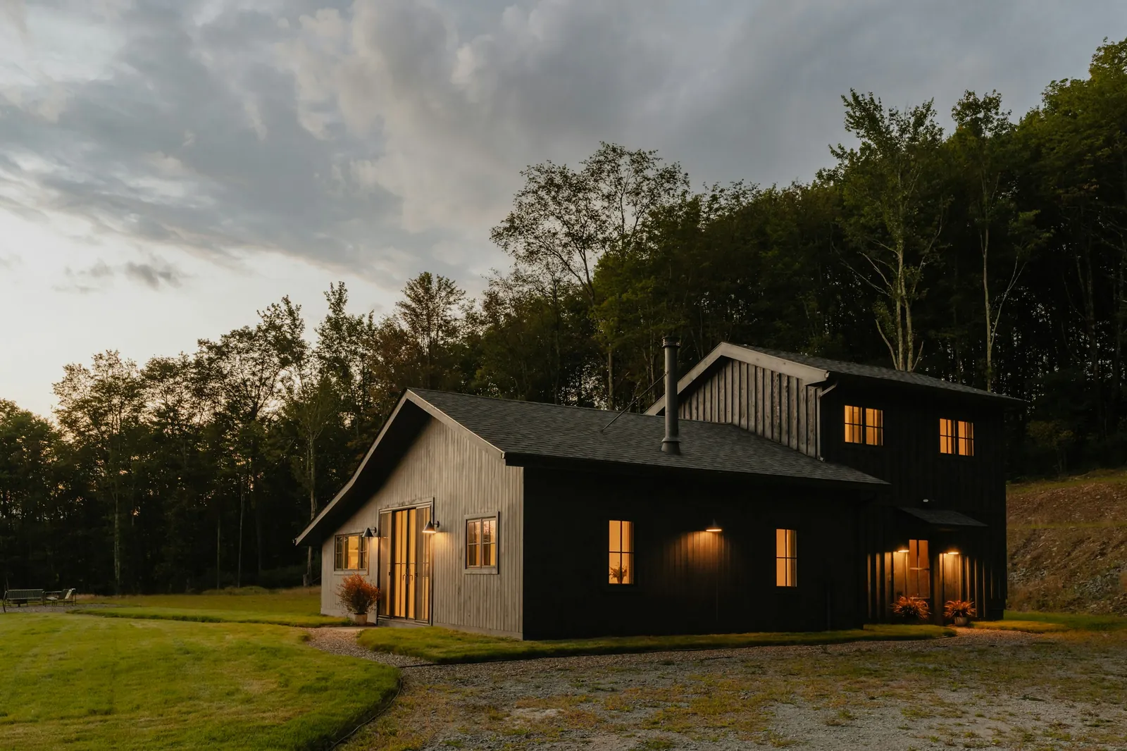 A black timber house at dusk with its windows lit