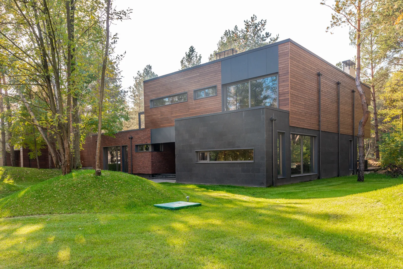 The house from the garden, timber cladding and a low dark wing
