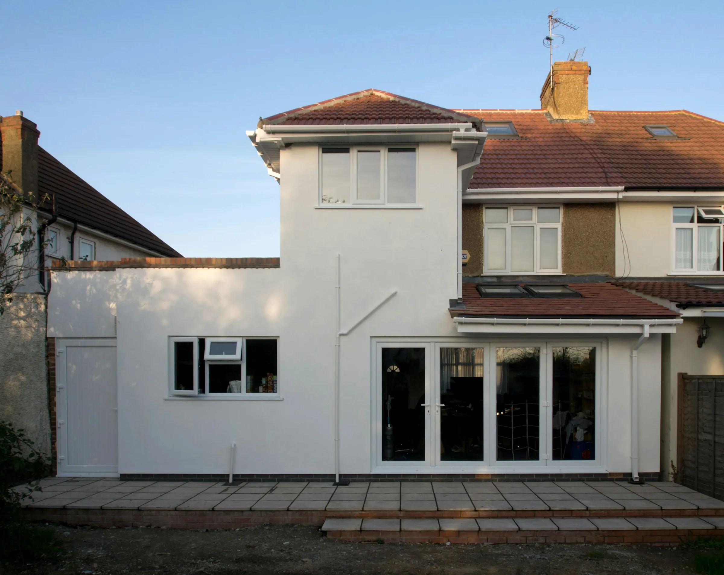 Lenton Villa: a rendered single-storey extension across the back of a 1930s semi, with folding doors onto a stone terrace
