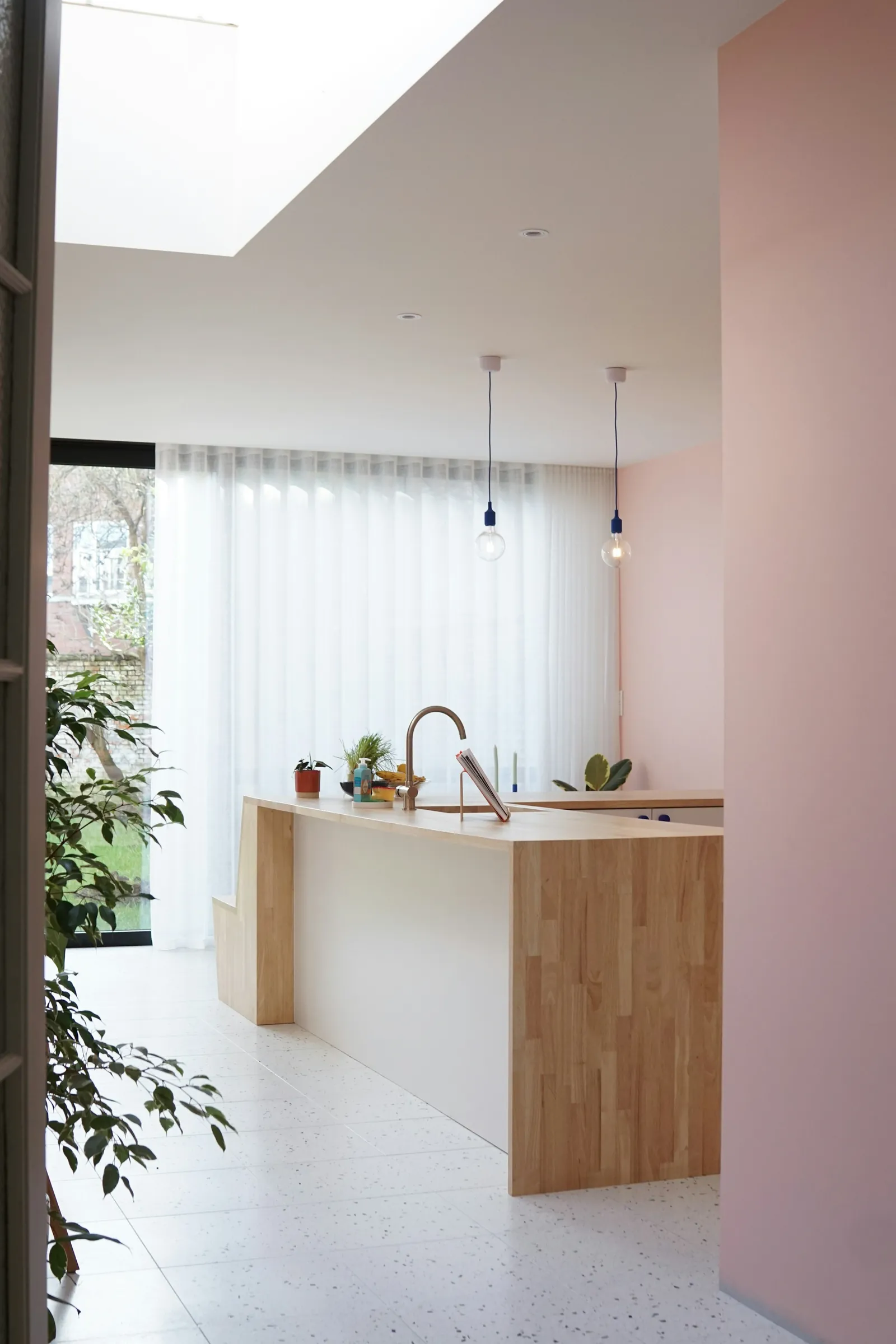 An oak kitchen island under a rooflight, a pink-painted wall beyond