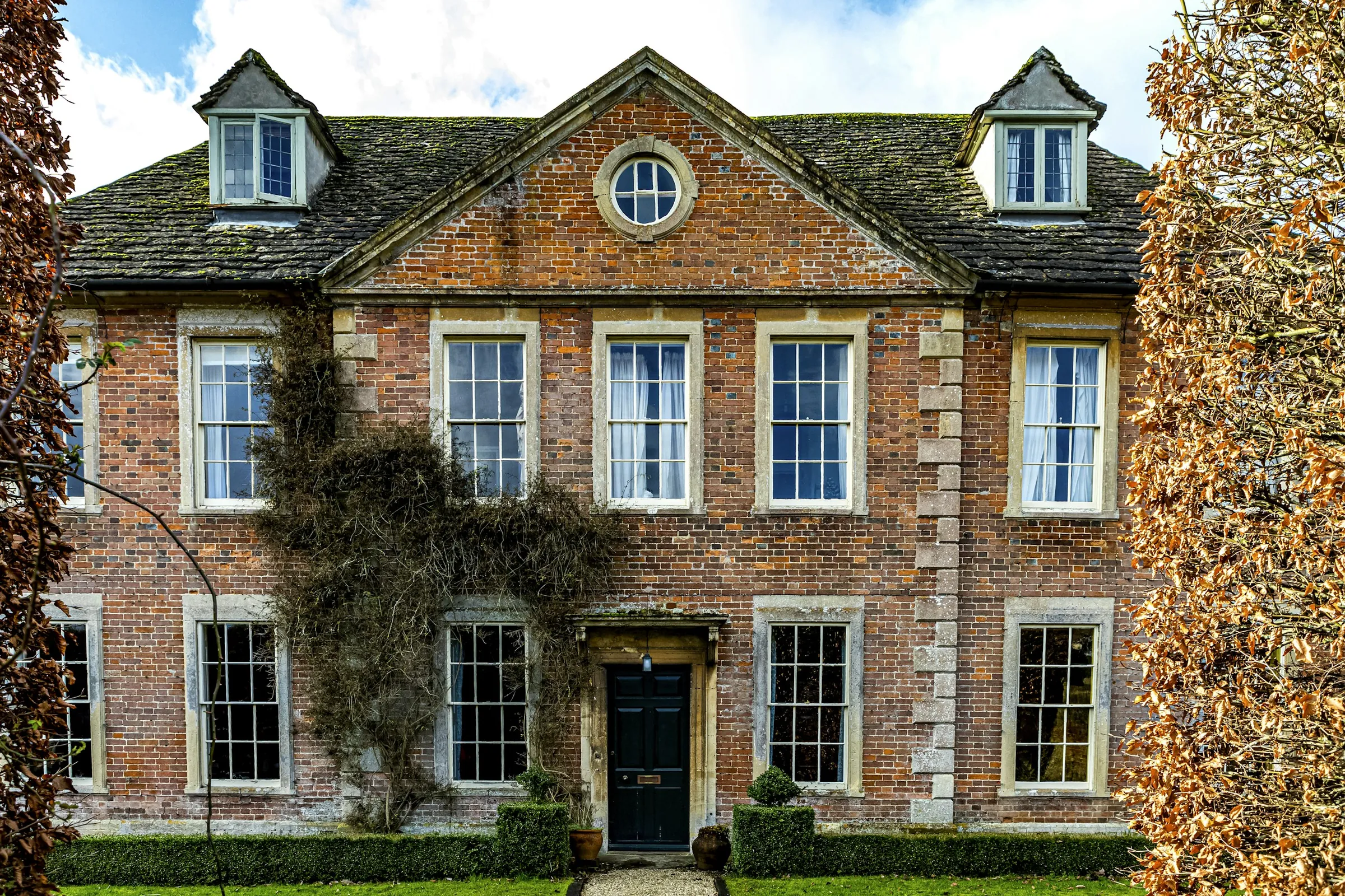 Manor Farm: a Georgian brick farmhouse with stone quoins, ivy on the walls and a black front door