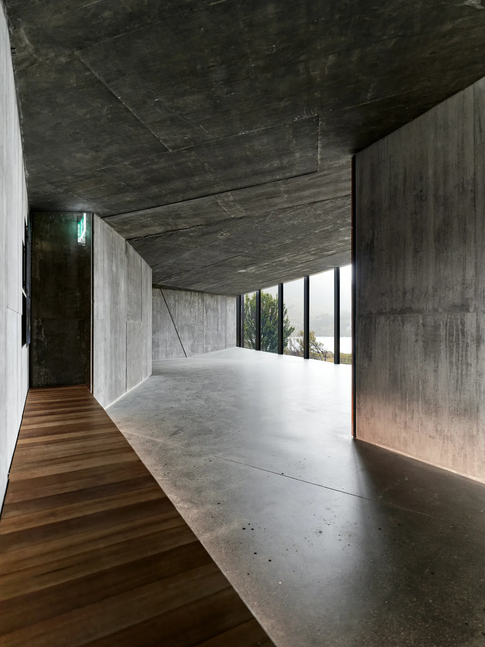 A board-marked concrete wall meeting a timber floor in a glazed hall