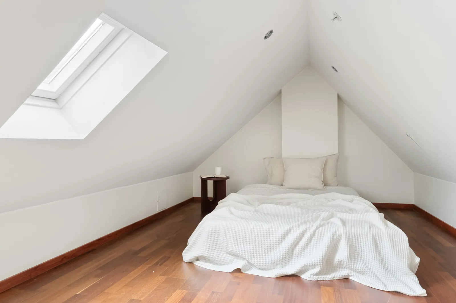 An attic bedroom with a white bed under a rooflight