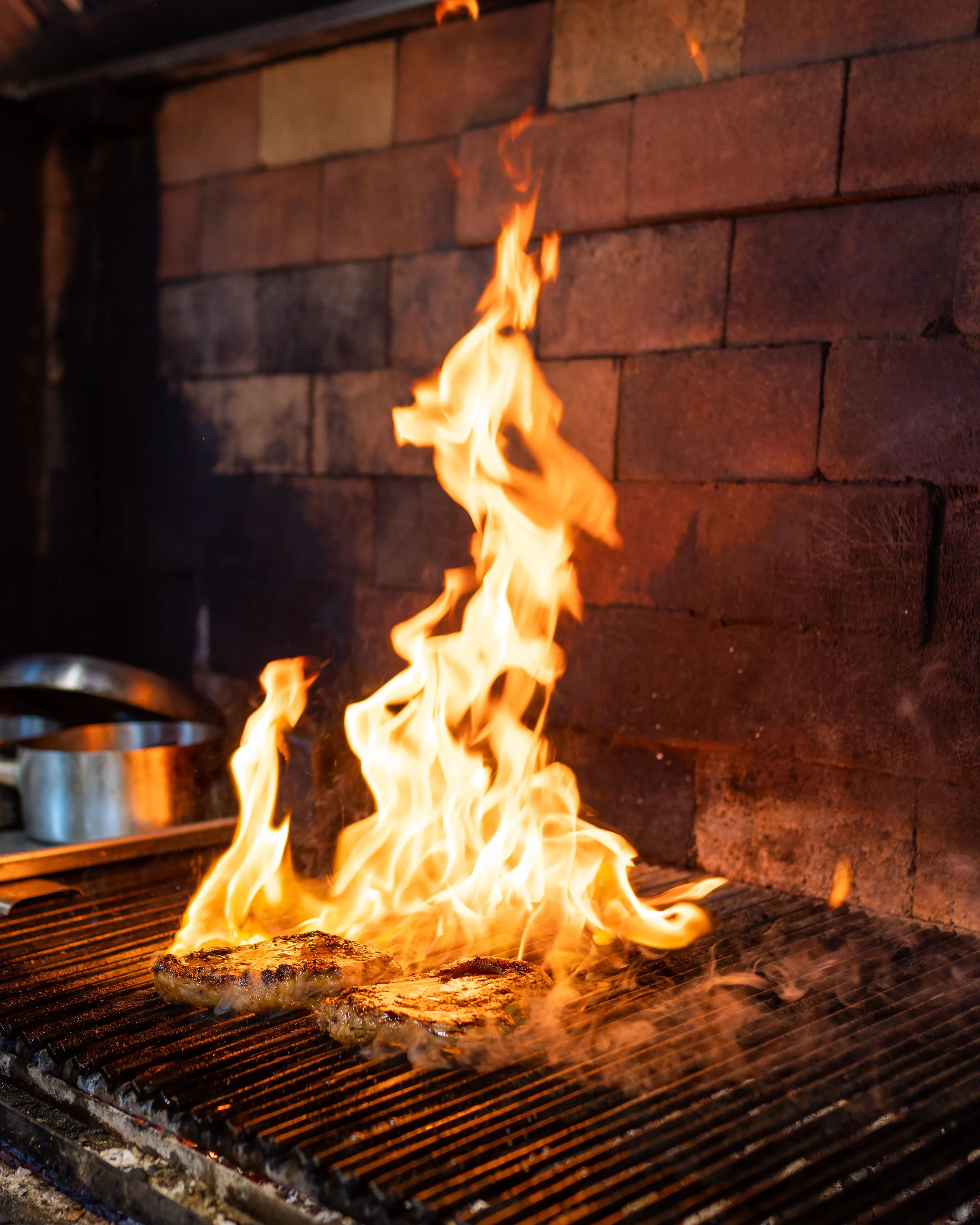 Flames leaping through the bars of a charcoal grill in a brick hearth