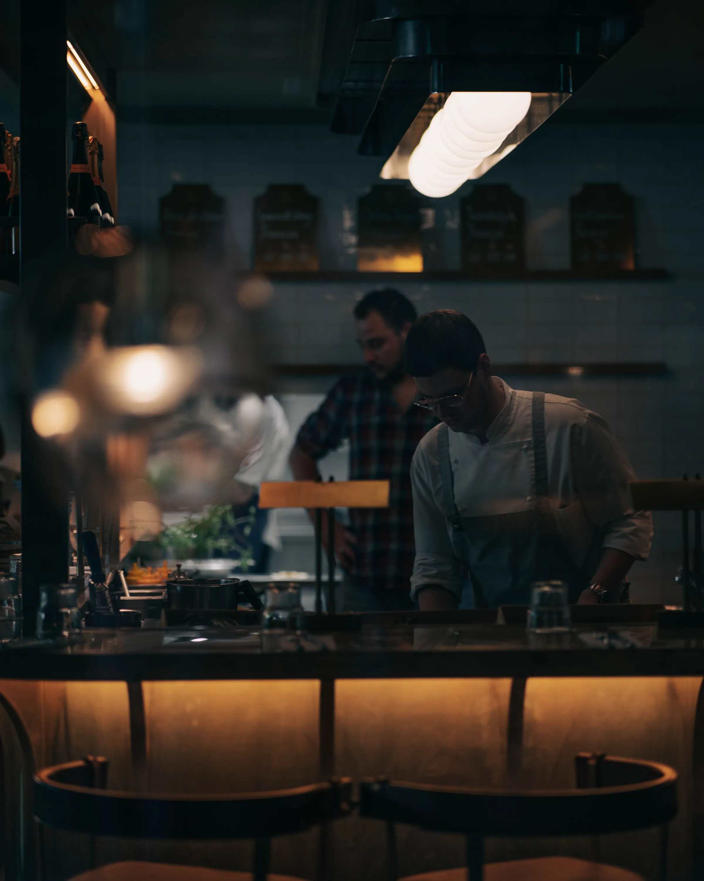Two chefs working behind the pass, seen over the counter stools
