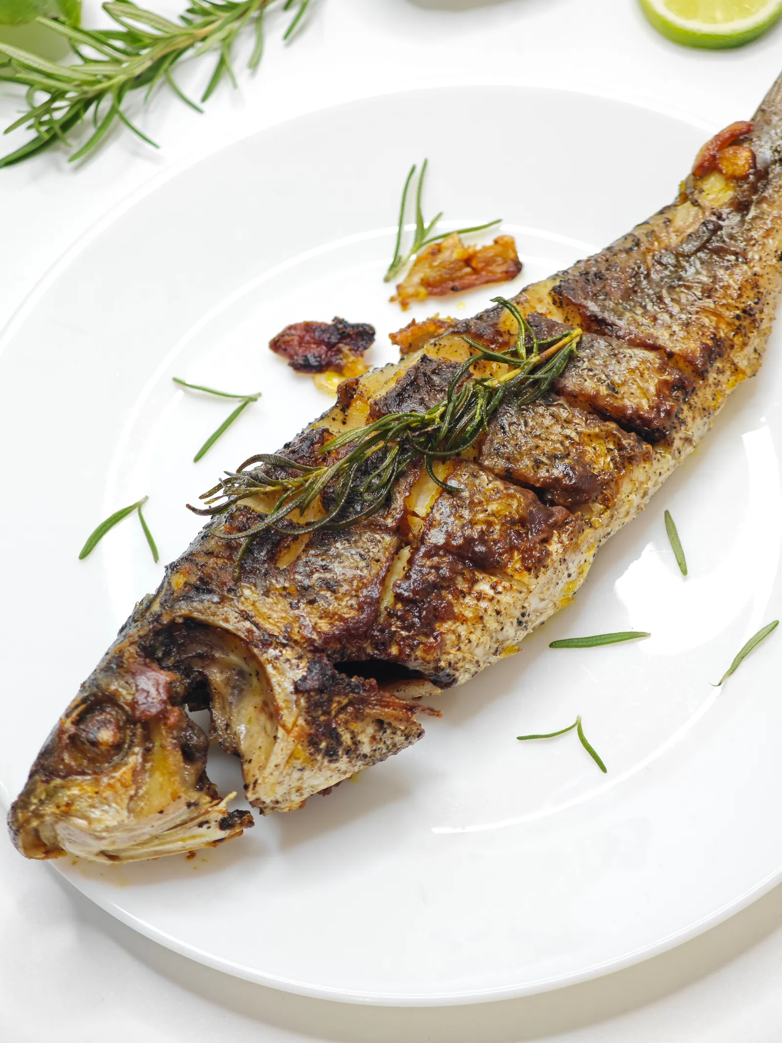 A whole sea bass, grilled, on a white plate with rosemary