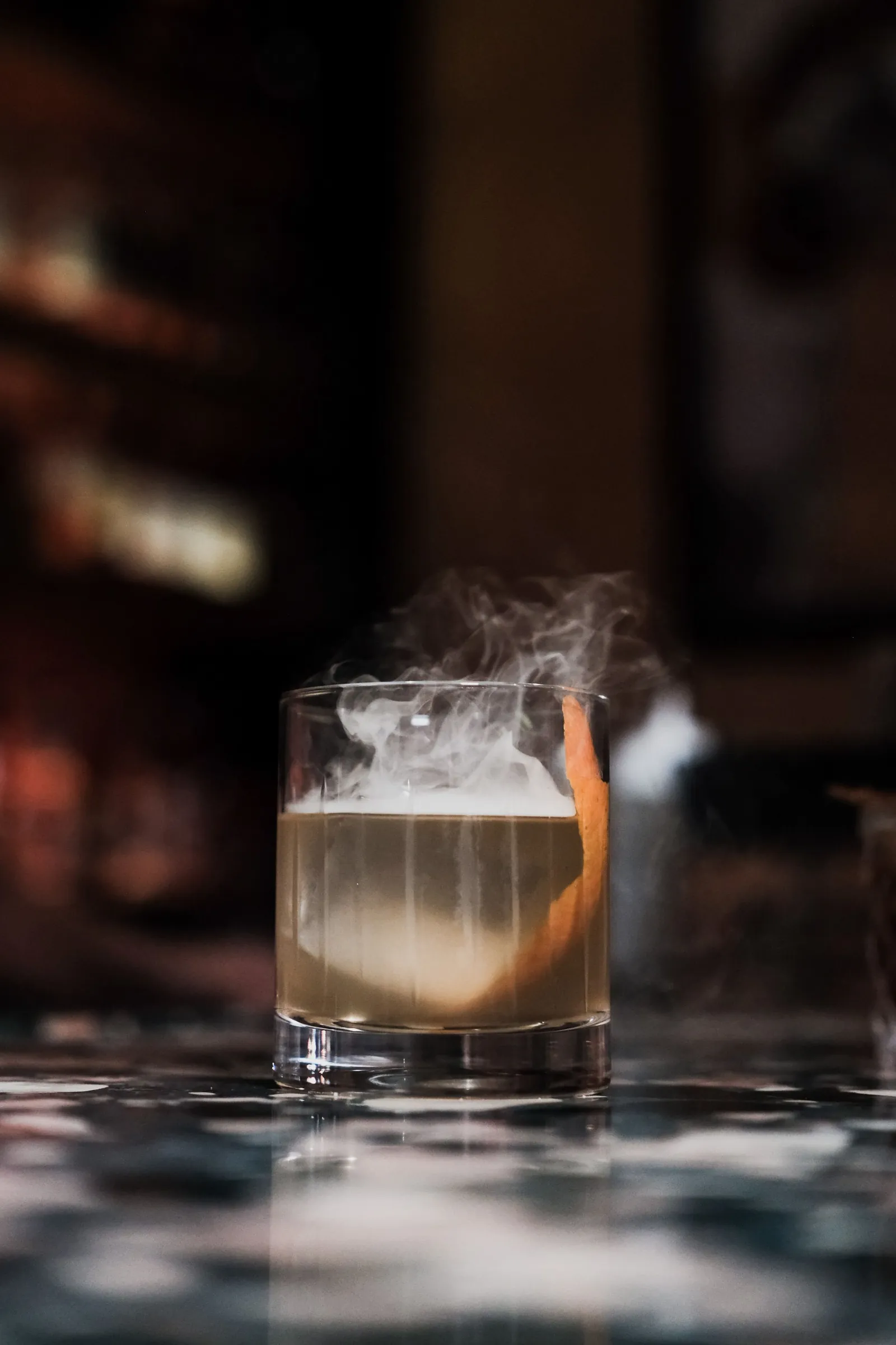 A cocktail under a cloud of smoke on a marble bar