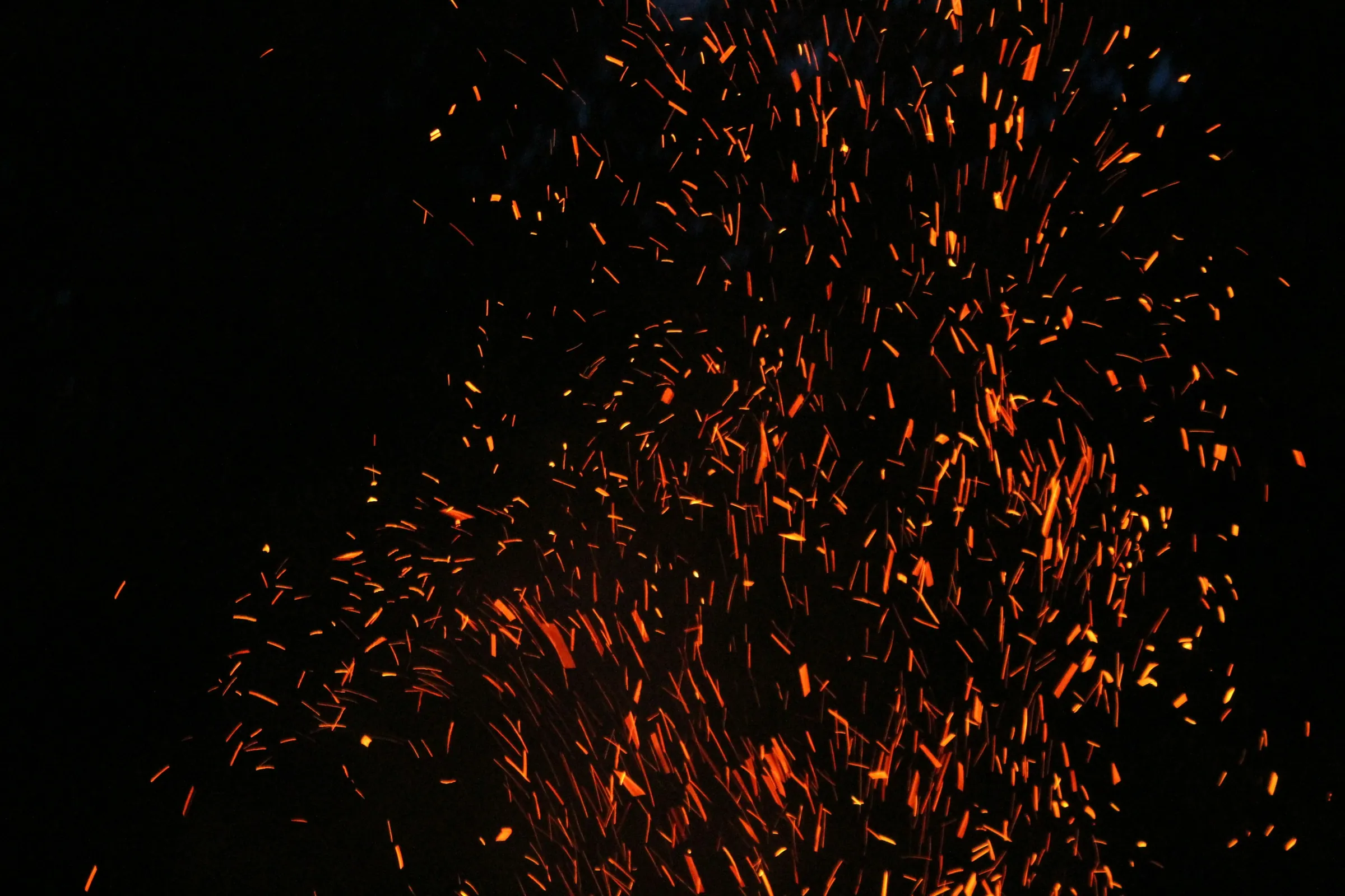 Orange sparks rising from a fire against a black sky