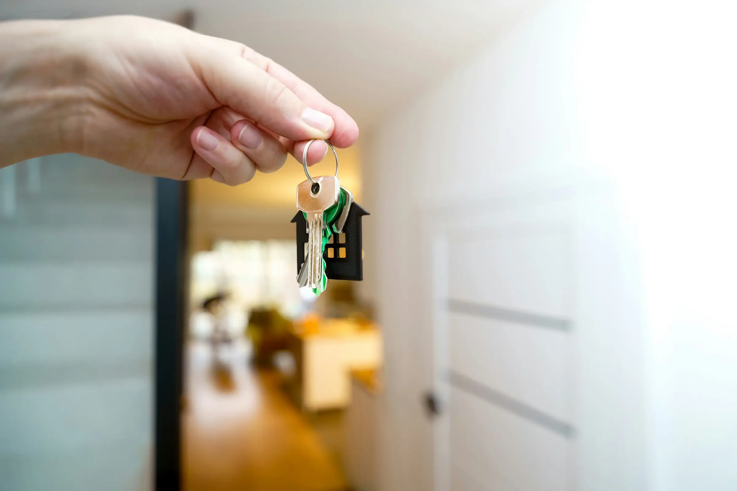 A hand holding a set of house keys in front of a front door