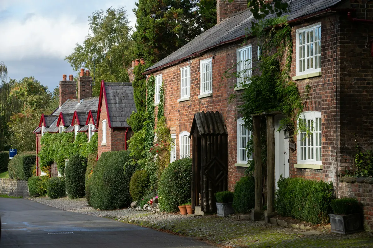 A row of brick village cottages with clipped hedges