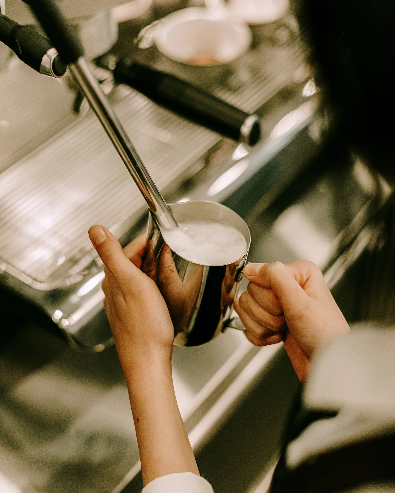 A barista steaming milk in a copper jug at an espresso machine