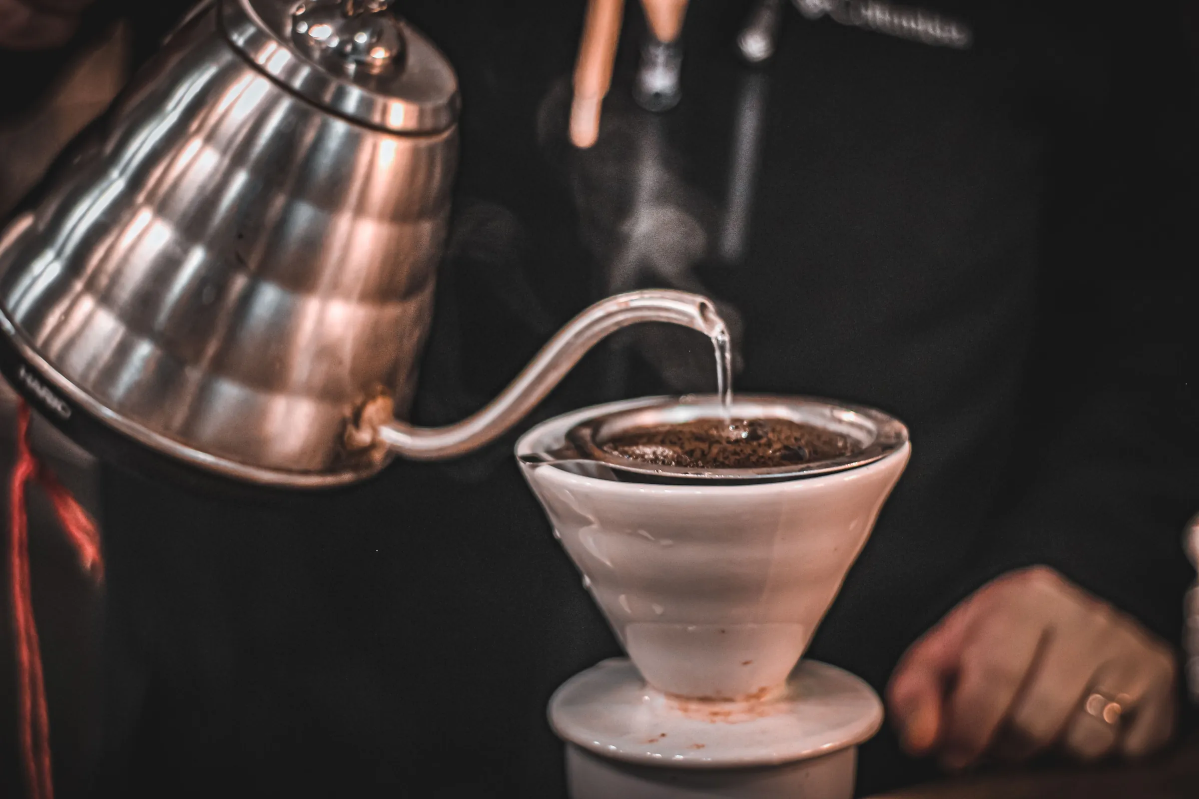 Water poured from a copper gooseneck kettle into a ceramic dripper, steam rising off the coffee bed