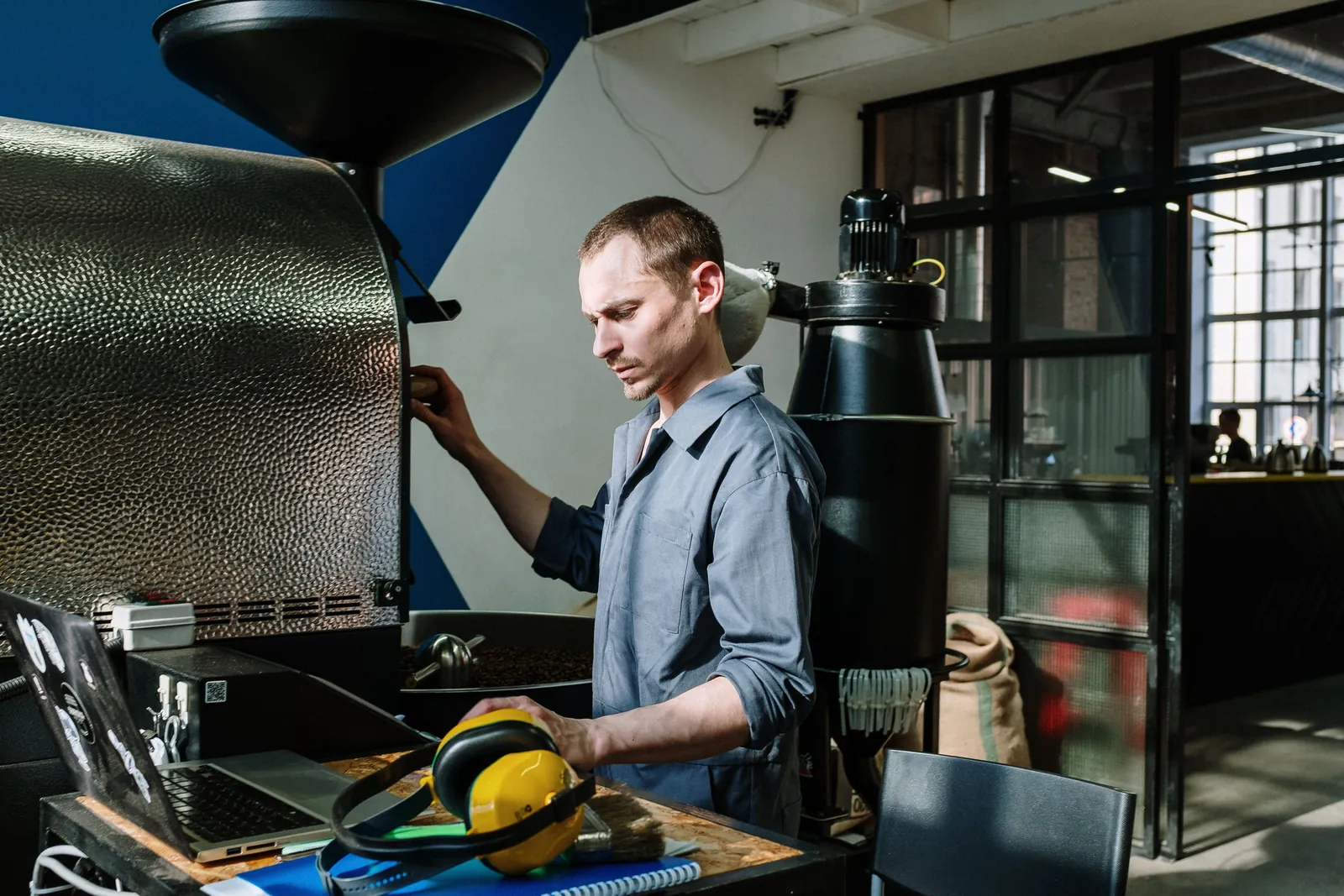 Kit checking the roast profile on a laptop beside the drum roaster