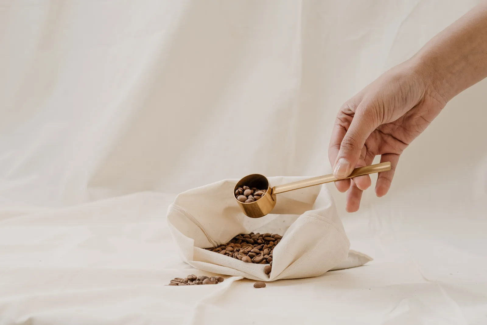 A hand scooping roasted beans from a plain cloth bag on white linen