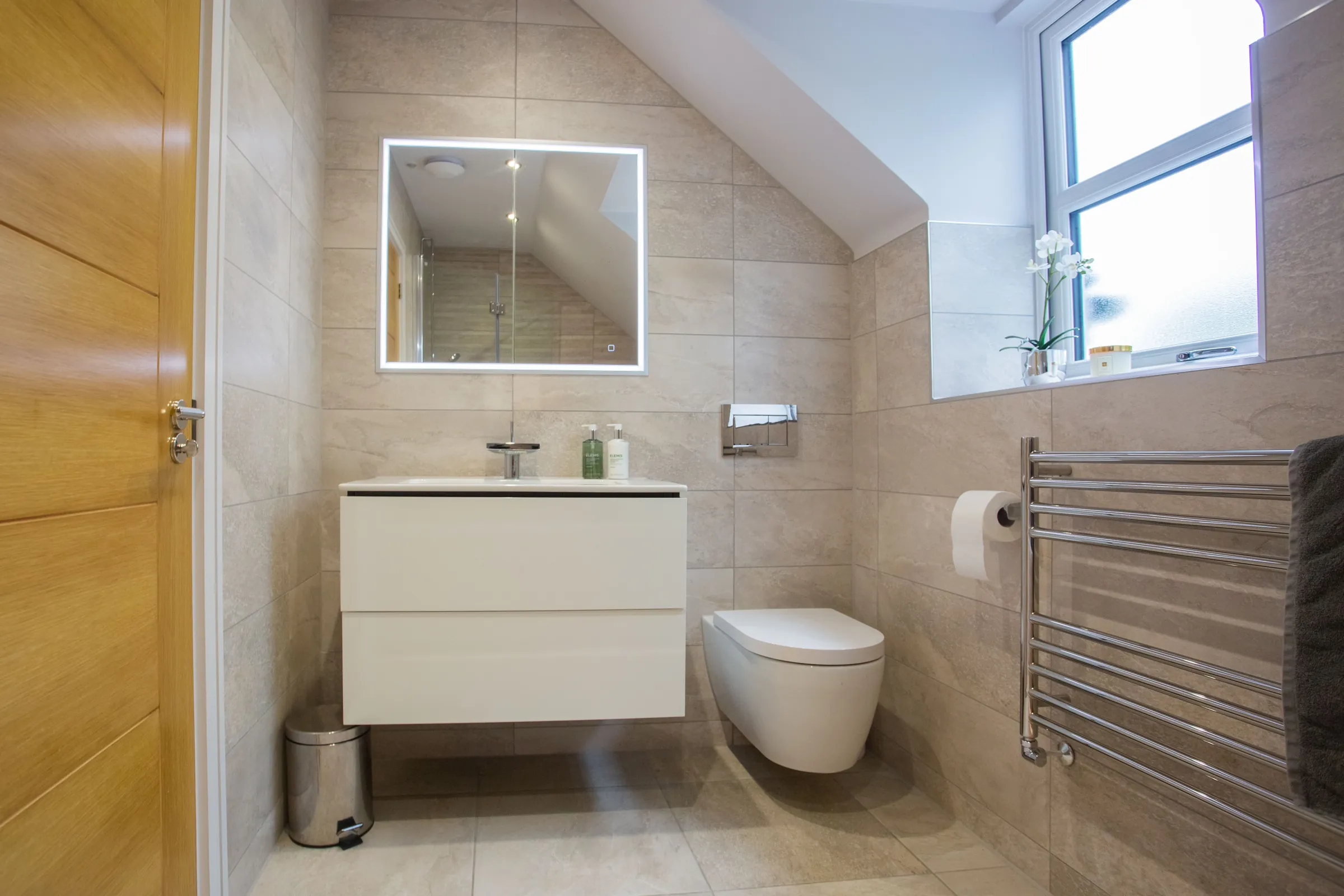 A finished bathroom with a wall-hung toilet, floating vanity and a heated towel rail