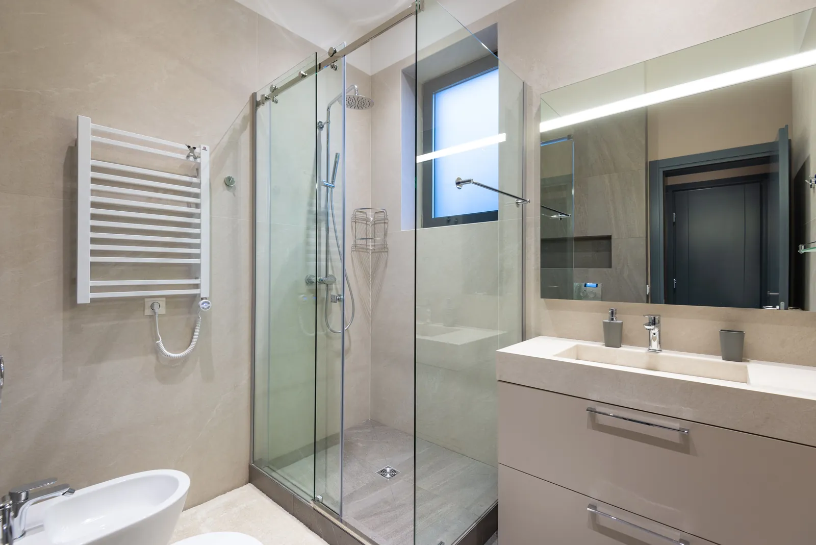 A bathroom with a glass shower enclosure, grey tiles and a white vanity