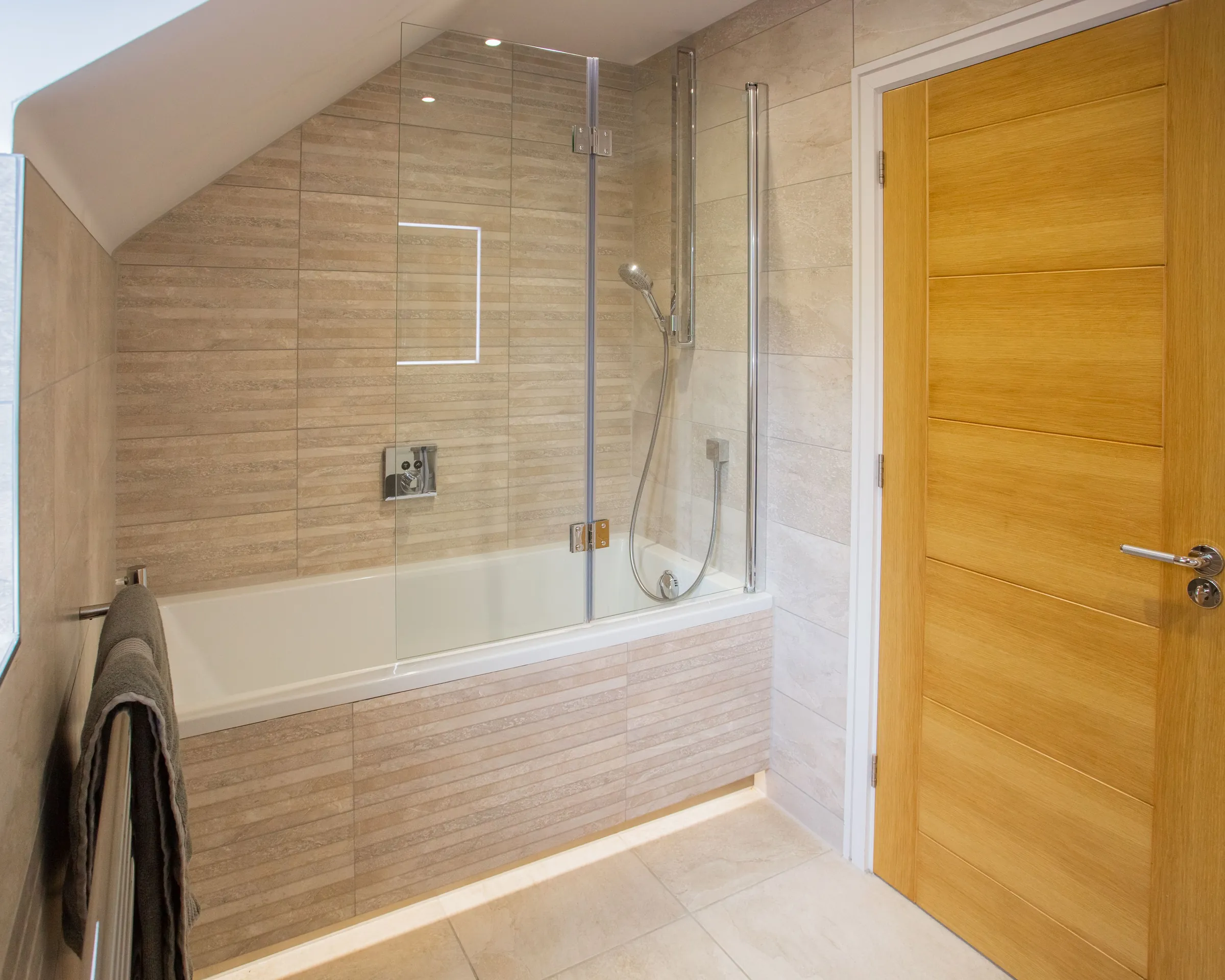 A finished bathroom with a bath, glass shower screen and stone-effect tiles