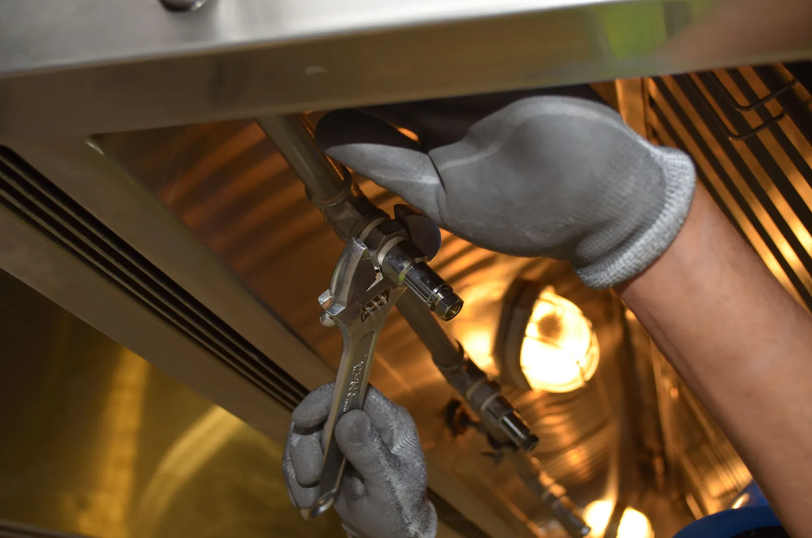 Gloved hands using a spanner on a fitting under a unit