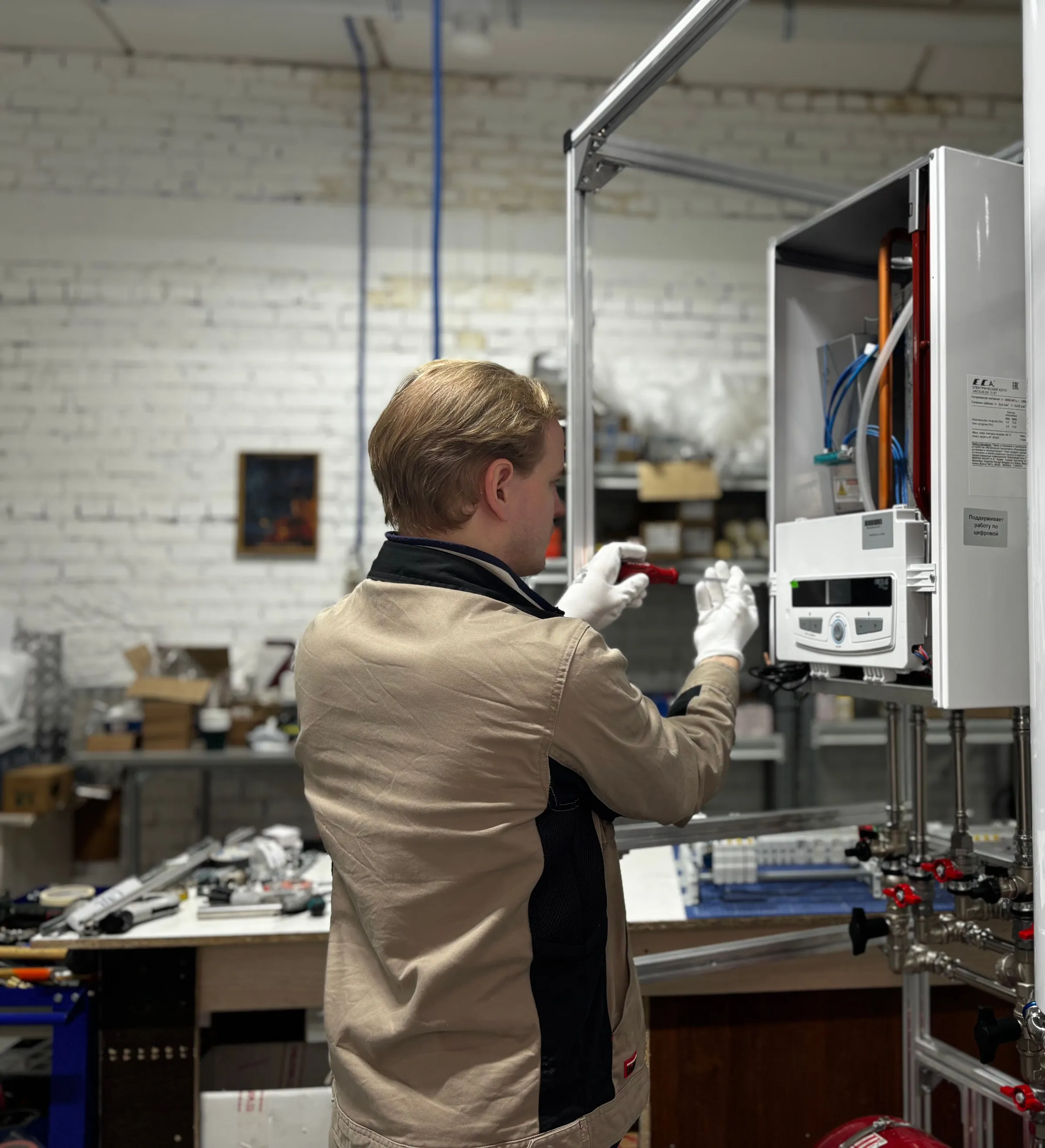An engineer in work gloves adjusting the controls on a wall-mounted gas boiler