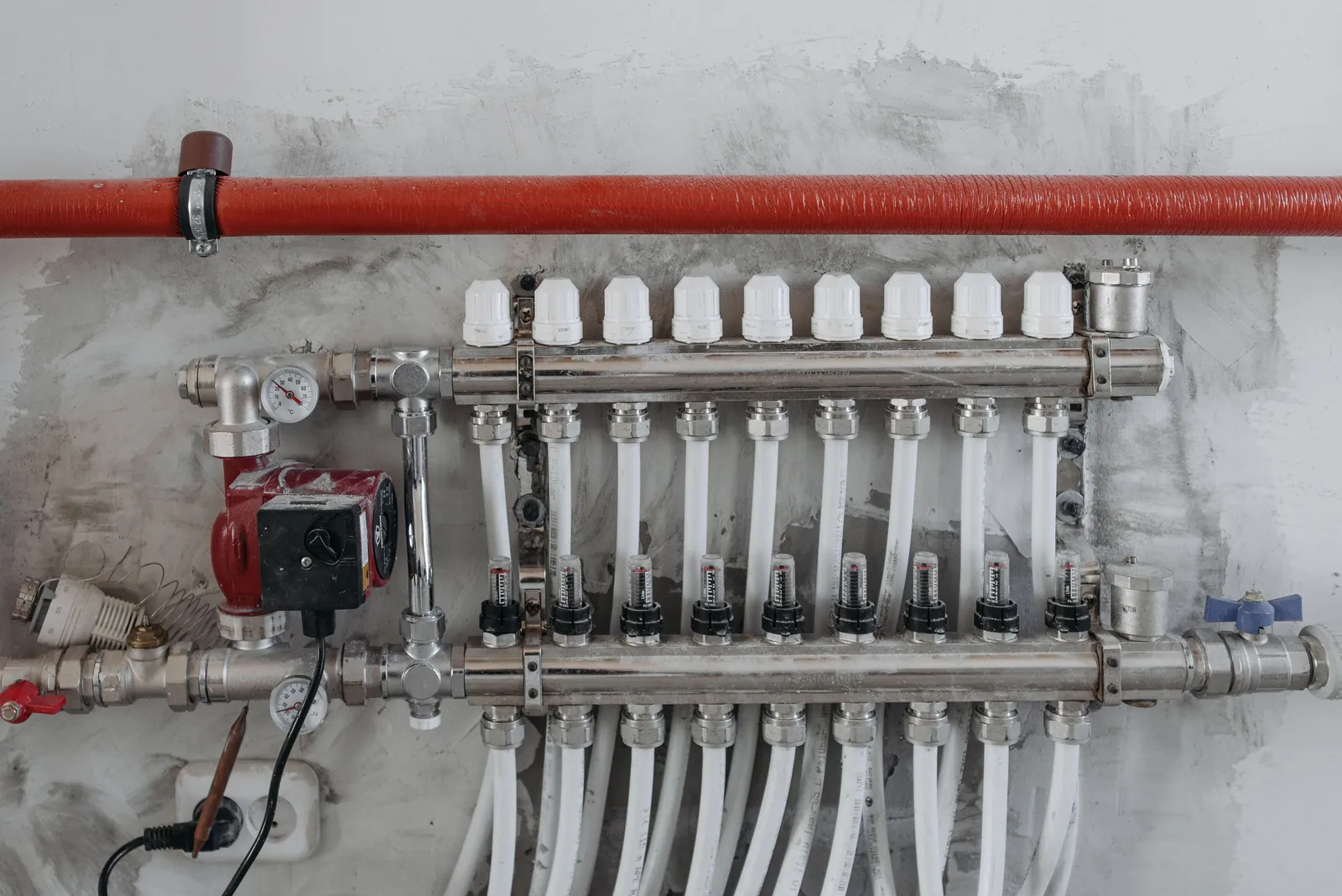 An underfloor heating manifold with red and white pipework on a wall