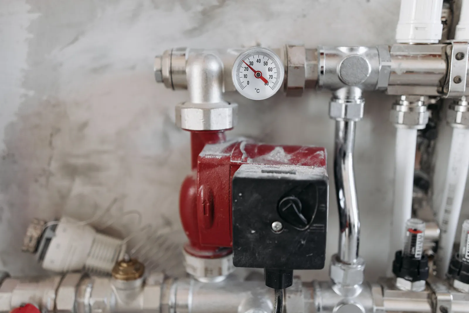 A heating manifold with pressure gauge and red pump on a plastered wall
