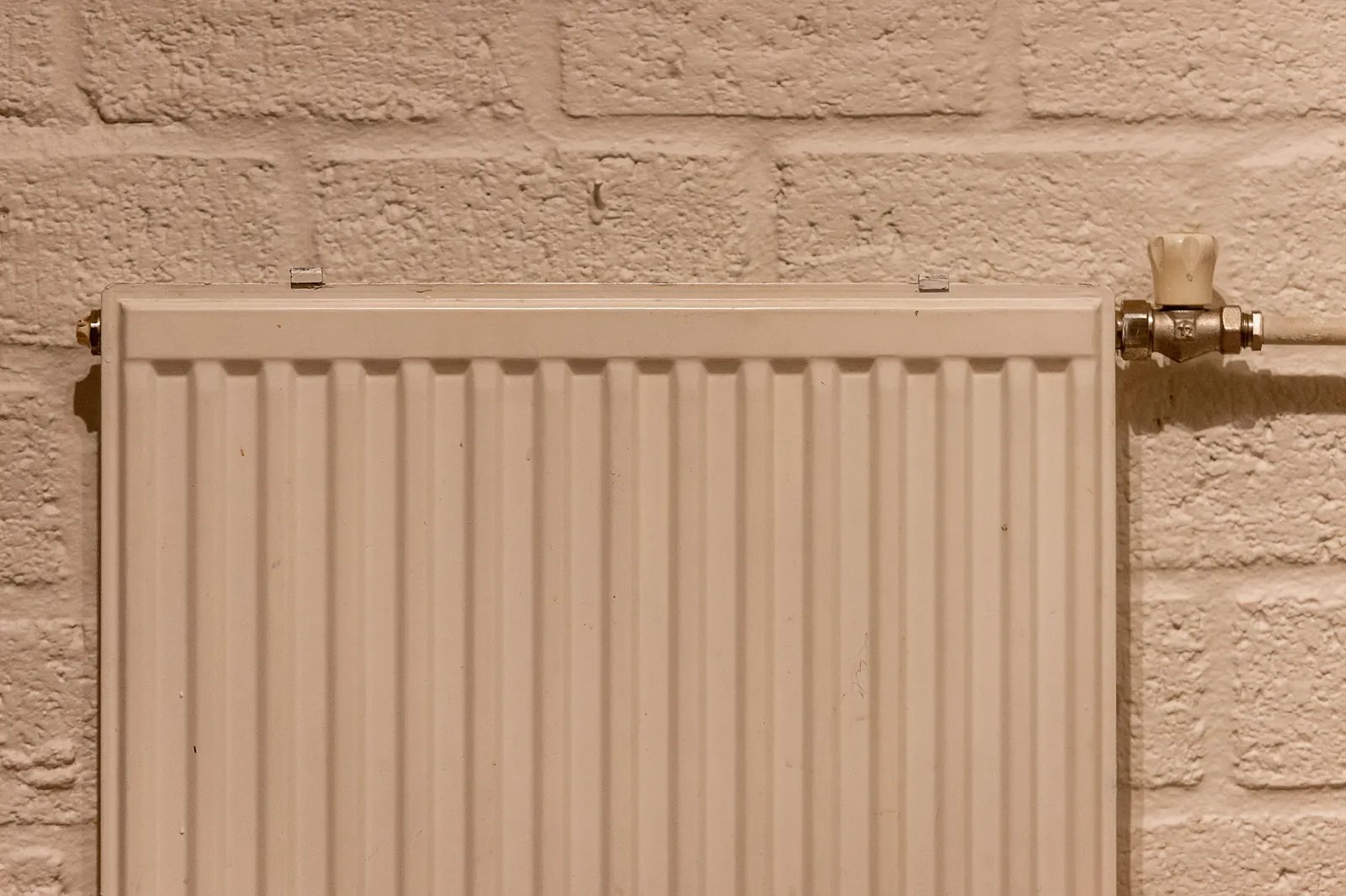 A white panel radiator on a painted brick wall in warm light