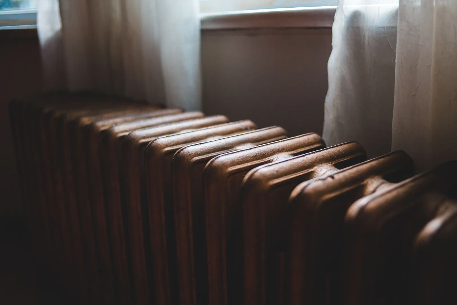 An old cast iron radiator under a window with net curtains