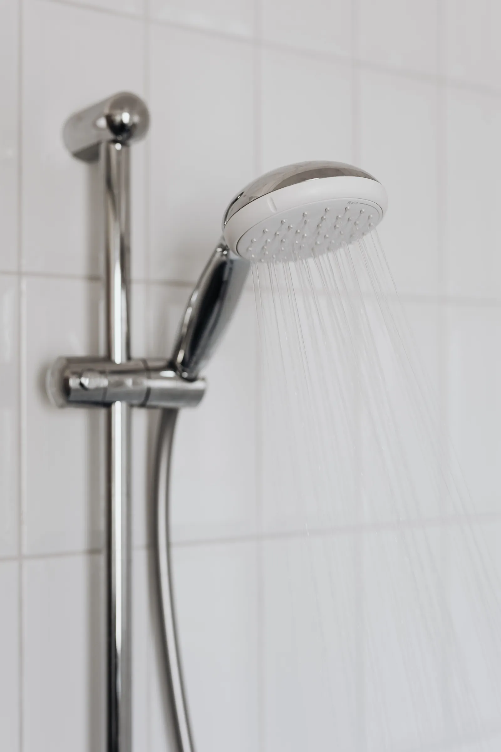 A chrome shower head and riser rail on white tiles