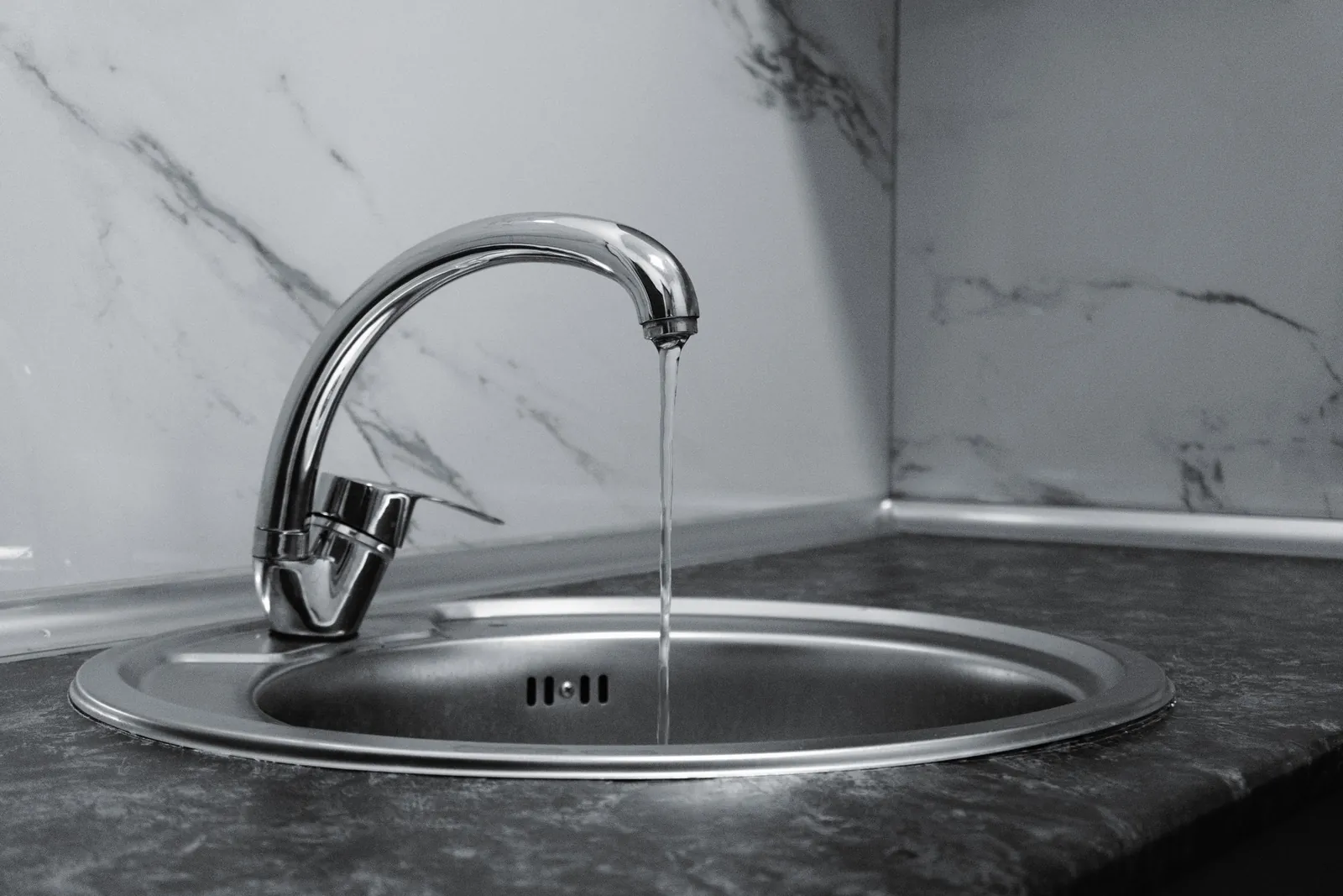 A chrome kitchen tap running into a stainless steel sink
