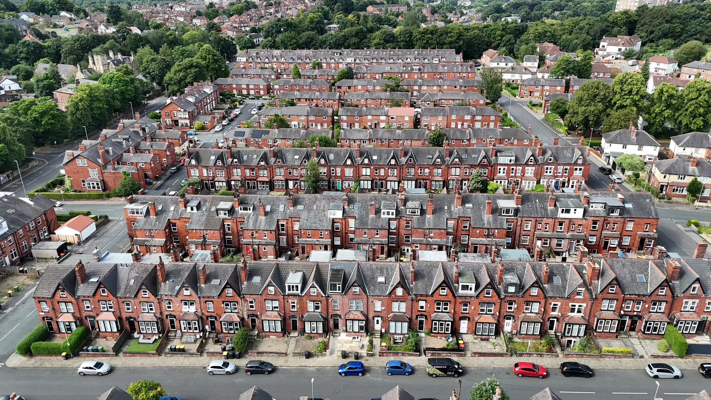 Rows of red brick terraced houses seen from above, with trees between the streets