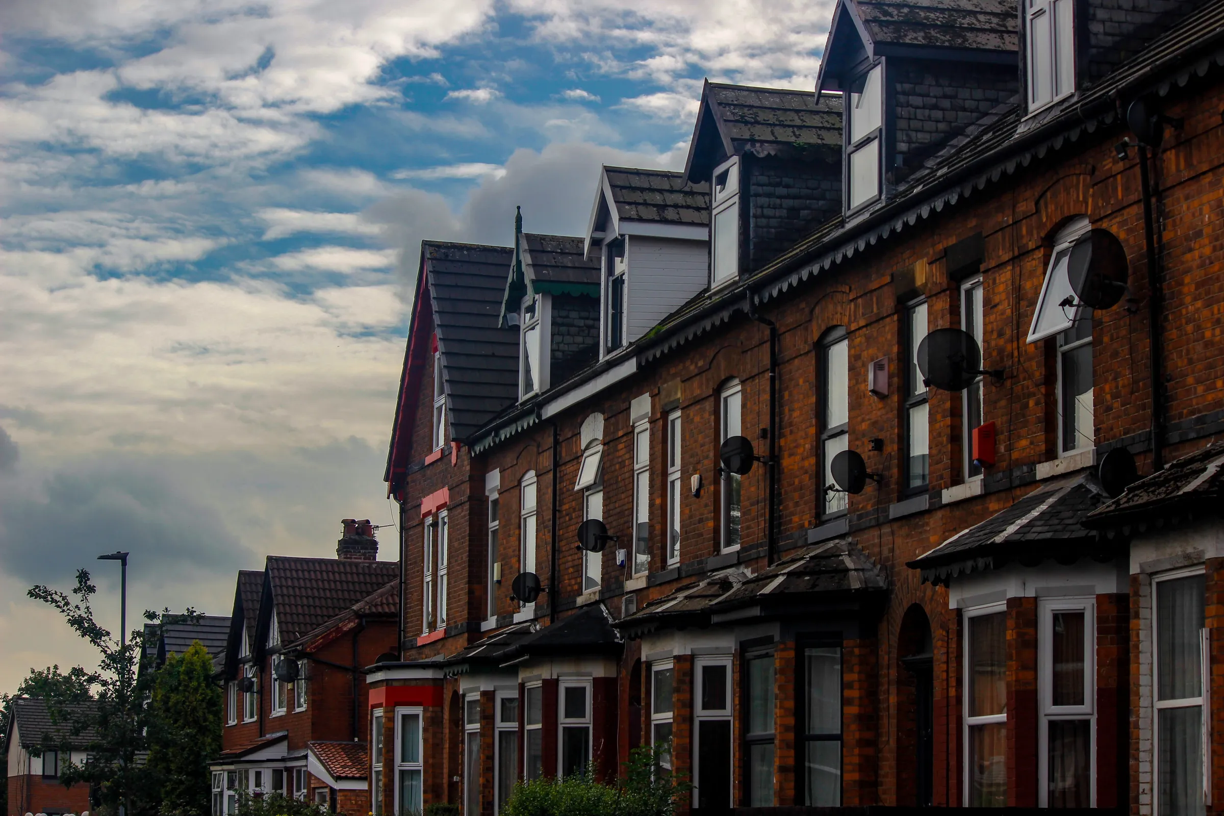 A row of red brick terraced houses with bay windows under a cloudy sky