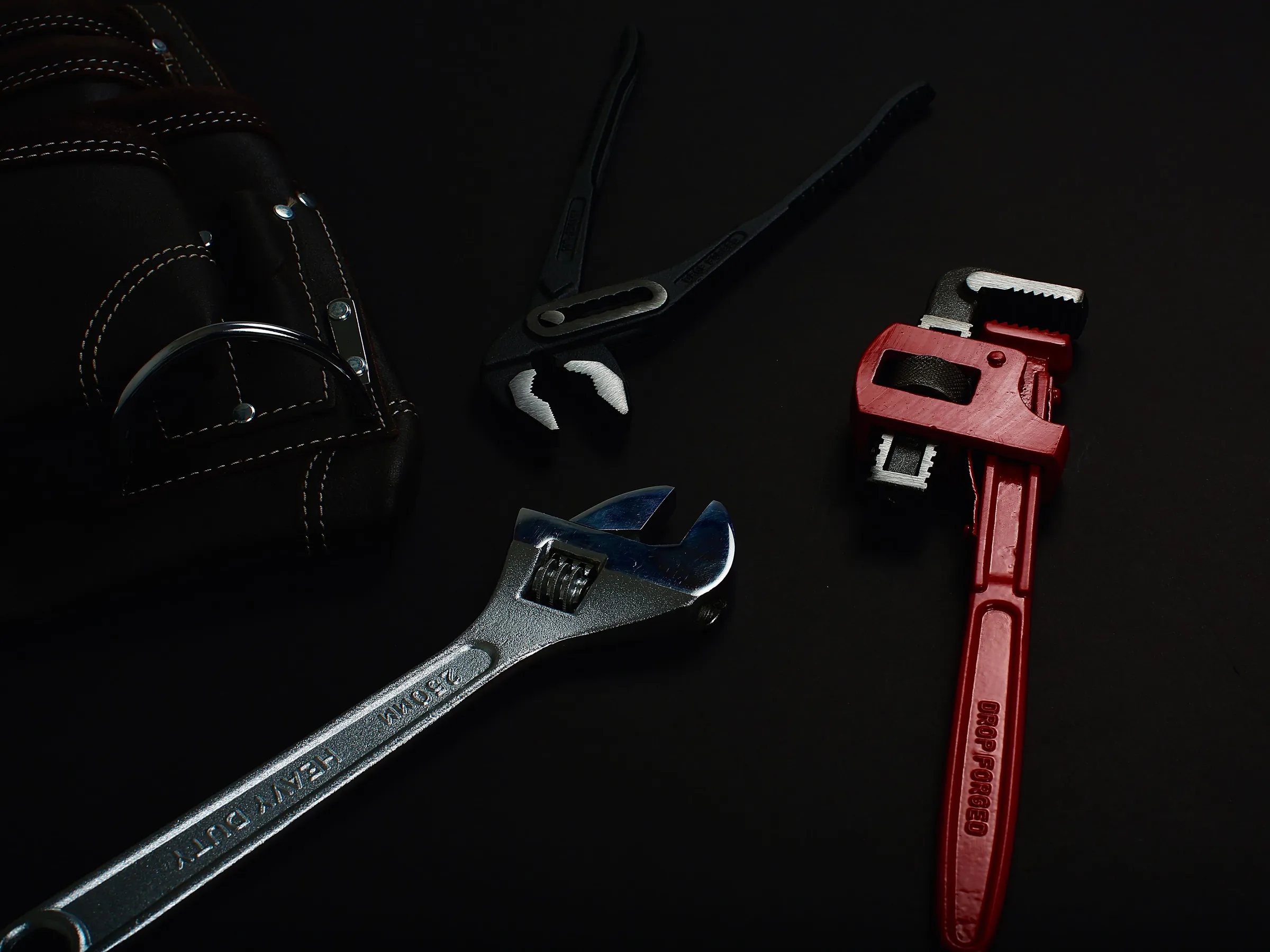 A pipe wrench, adjustable spanners and a leather tool roll on a dark surface