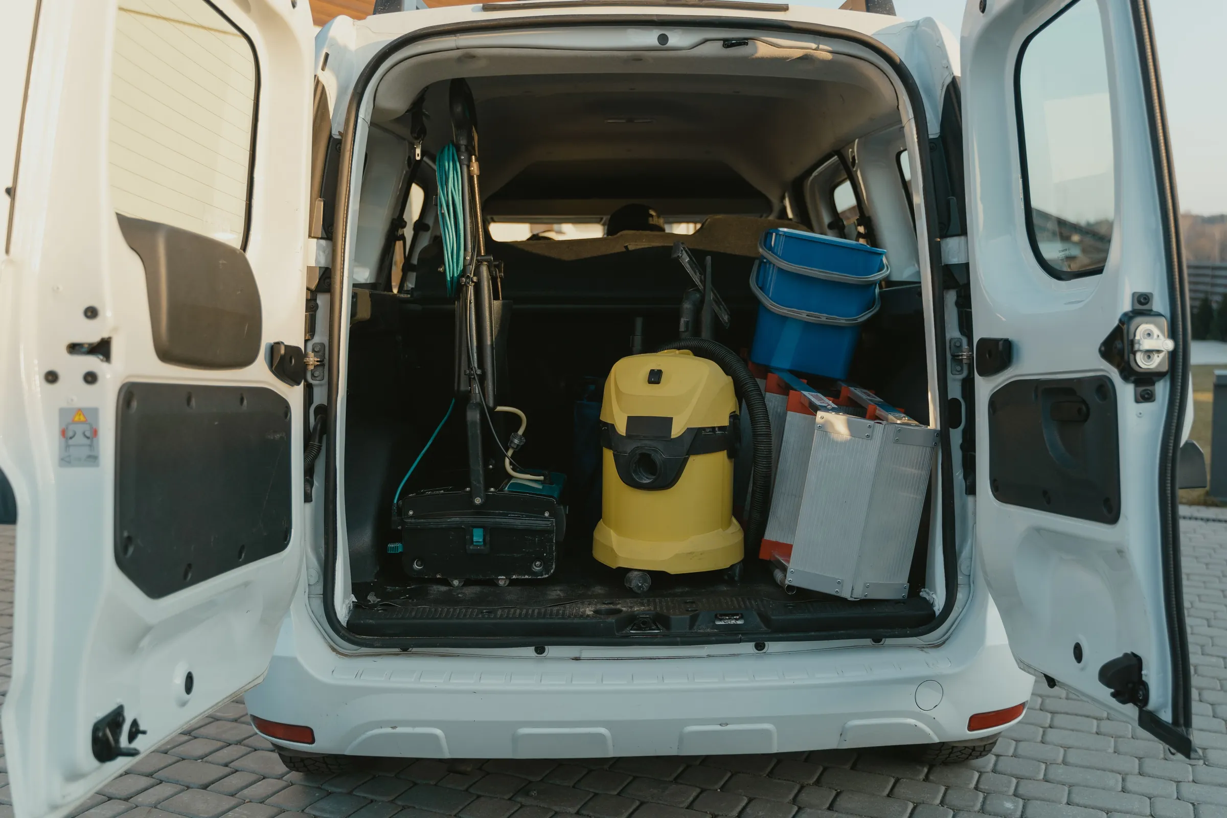 The open back of a white van with tools, a wet vacuum and crates loaded inside