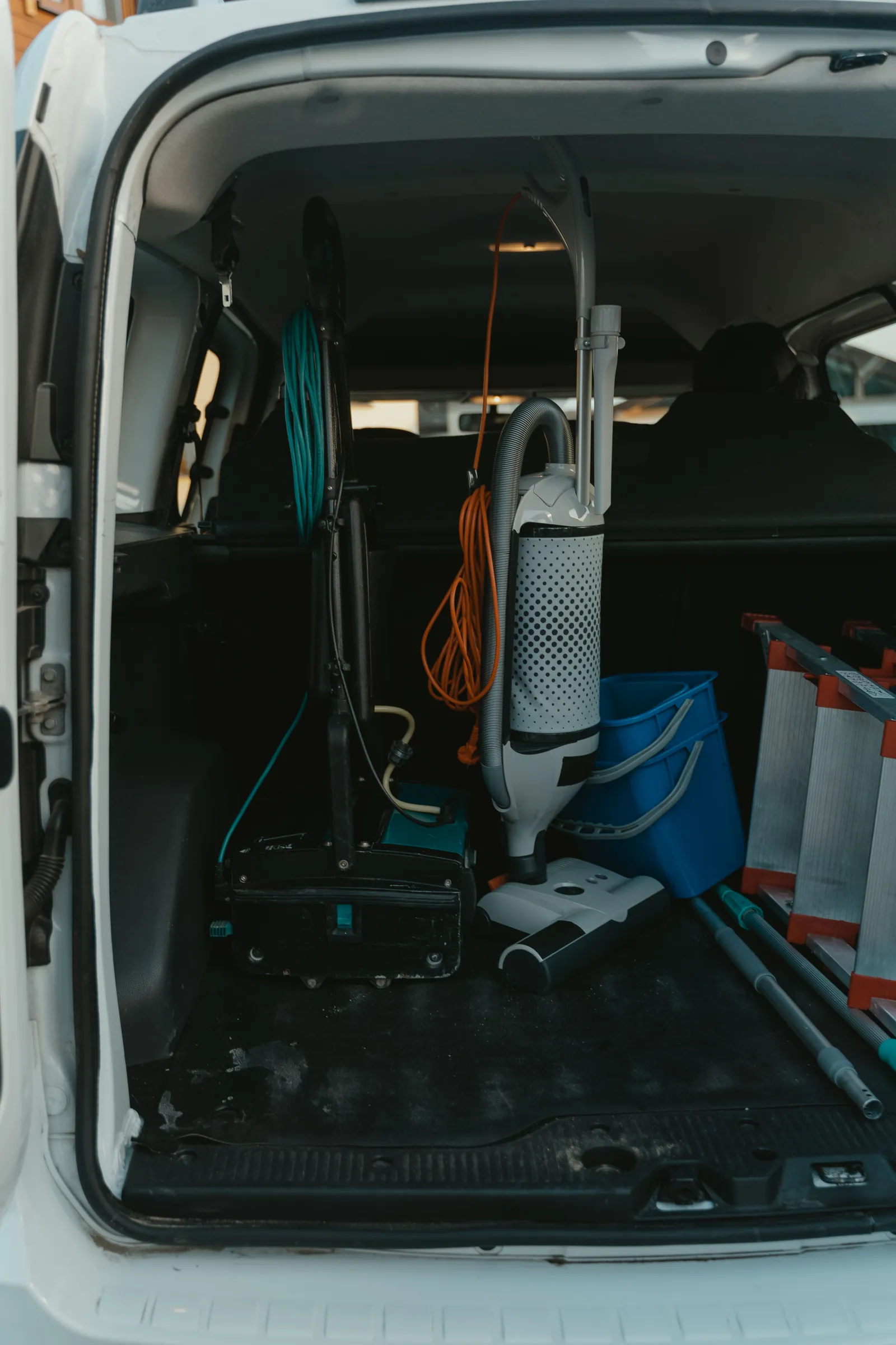 The back of a white van open on a driveway, shelves of tools and hoses inside