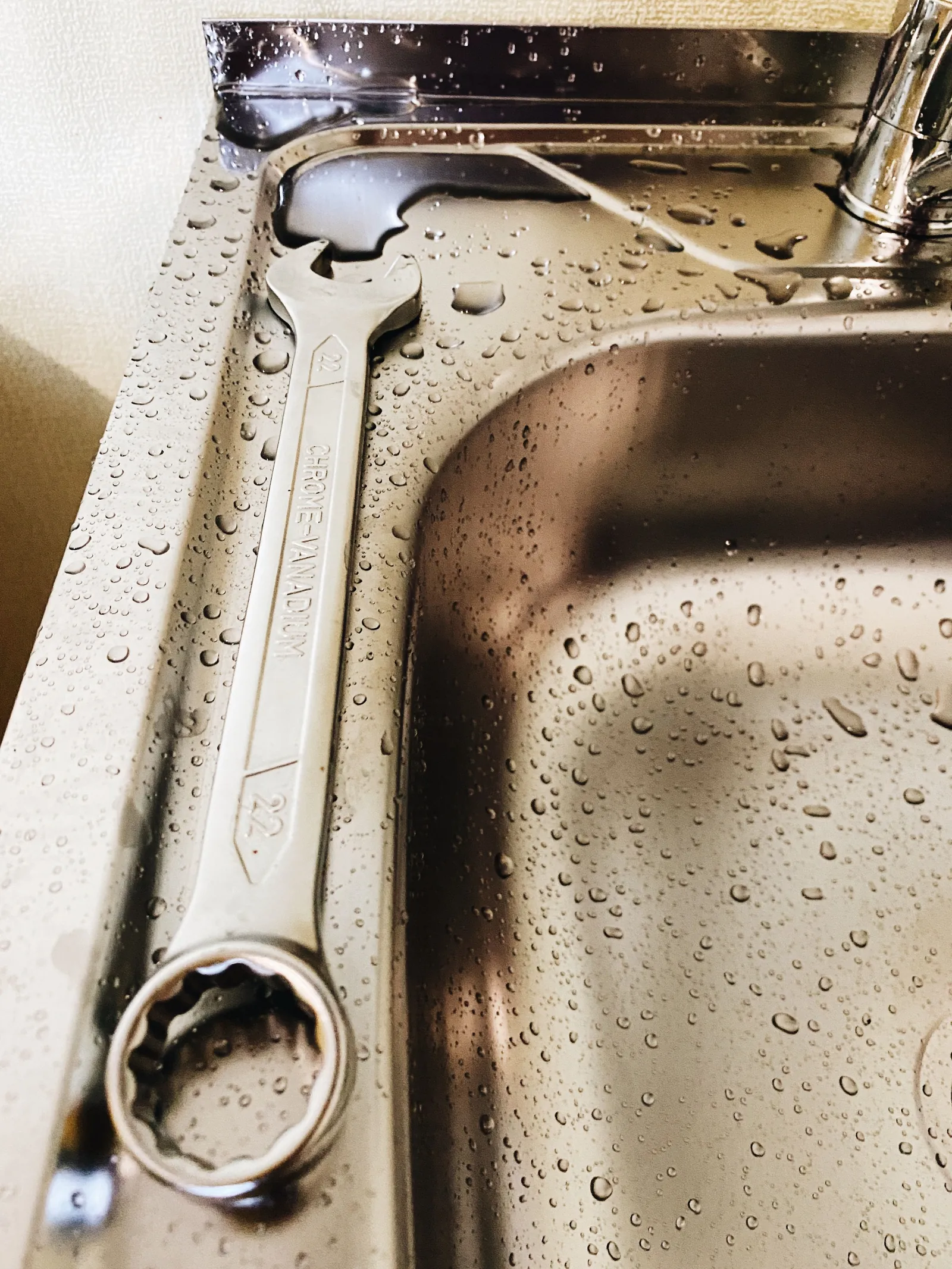 An adjustable spanner resting in a wet stainless steel sink