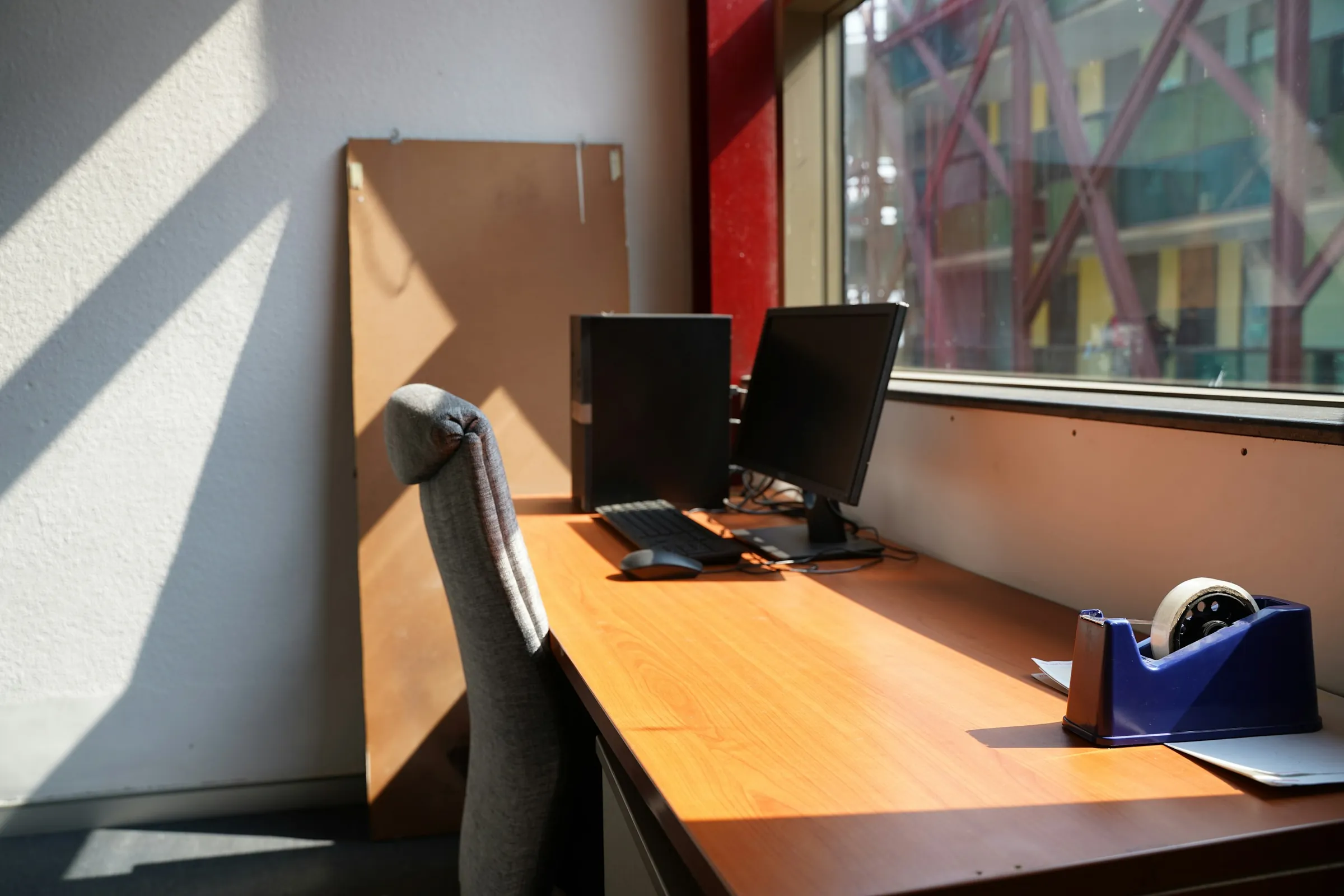 A desk by a sunlit window with a monitor, keyboard and a coffee cup