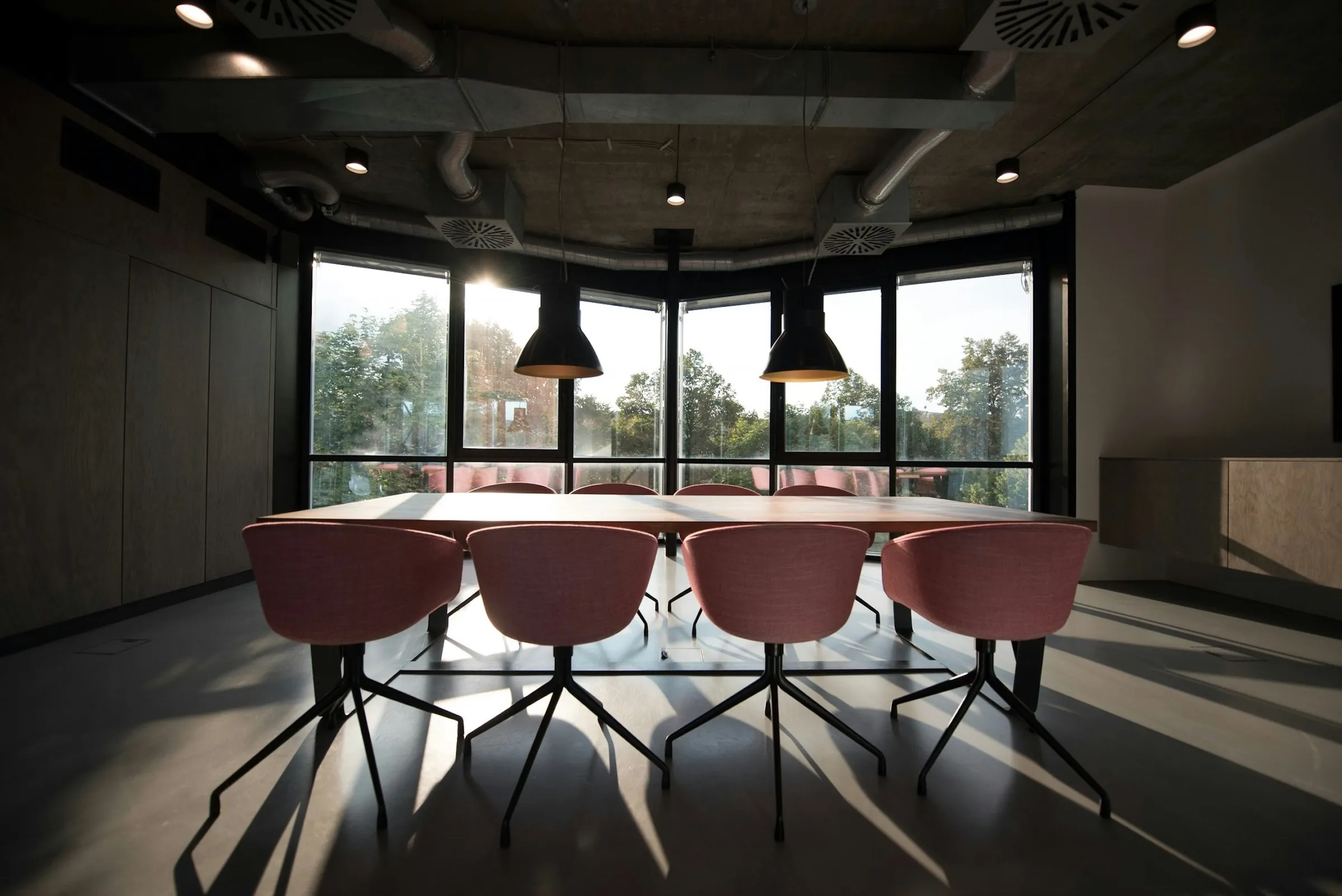 A meeting room with pink chairs around a light wooden table