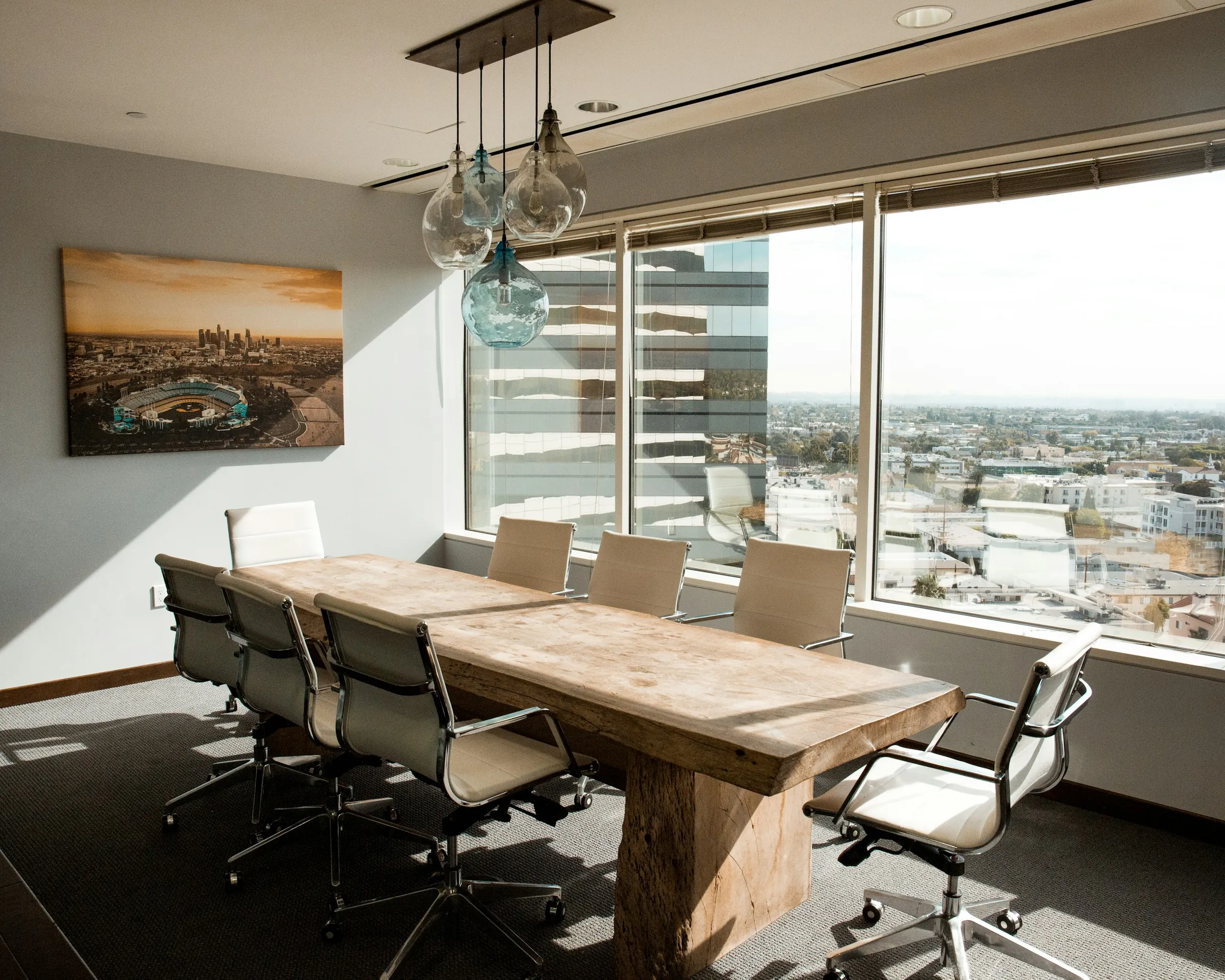 A long wooden meeting table with white chairs beside a window looking out over the town
