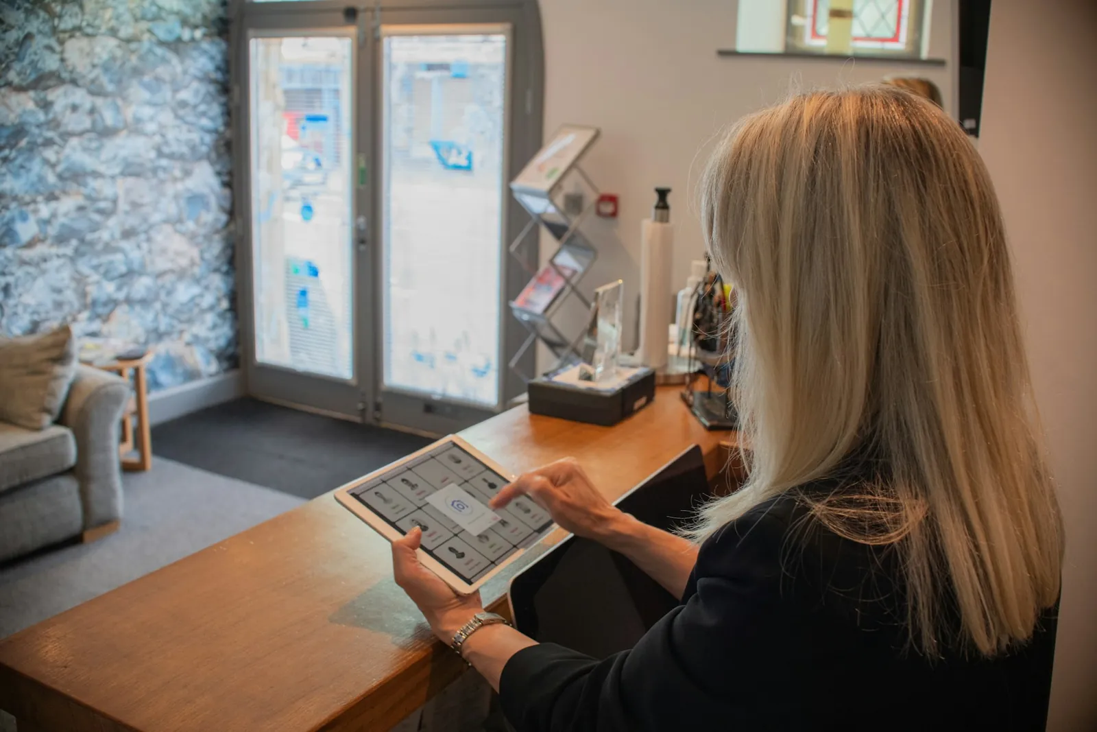 A receptionist at a wooden front desk using a tablet