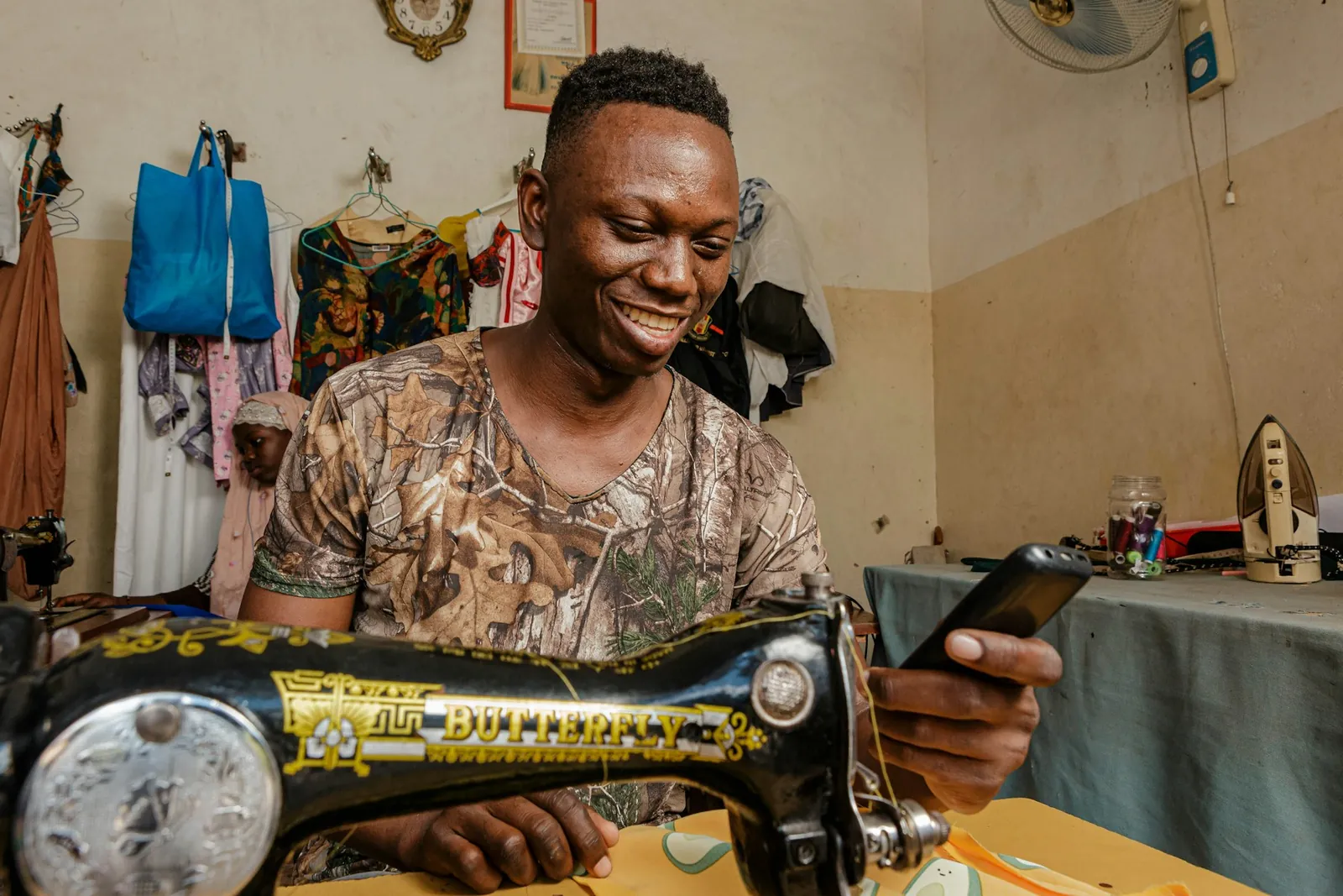 A tailor at his sewing machine, smiling as he works