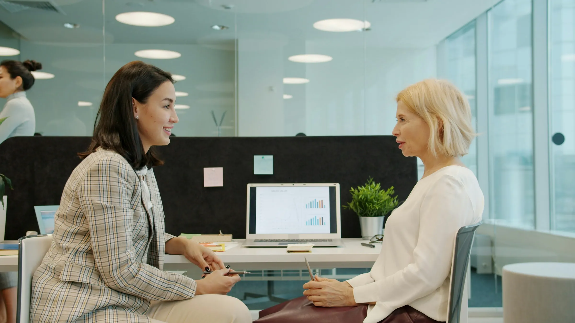 Two colleagues talking across a desk in a bright office