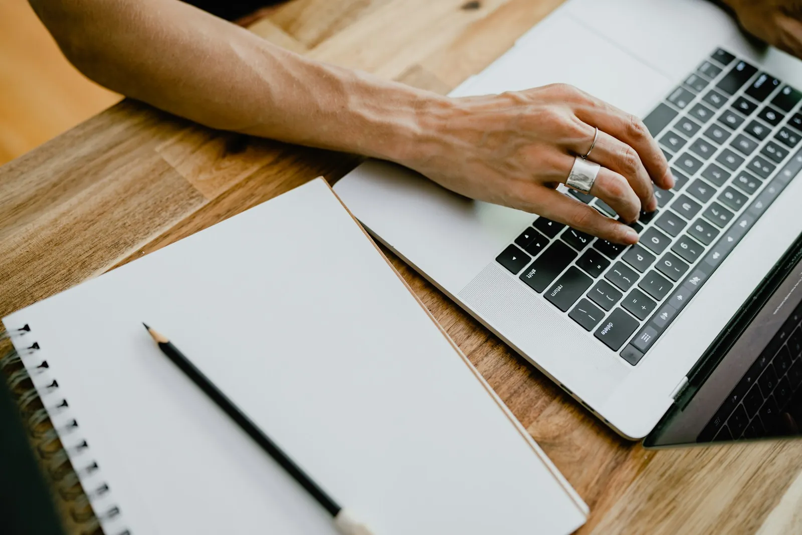 Hands typing on a laptop with a pencil and notebook alongside