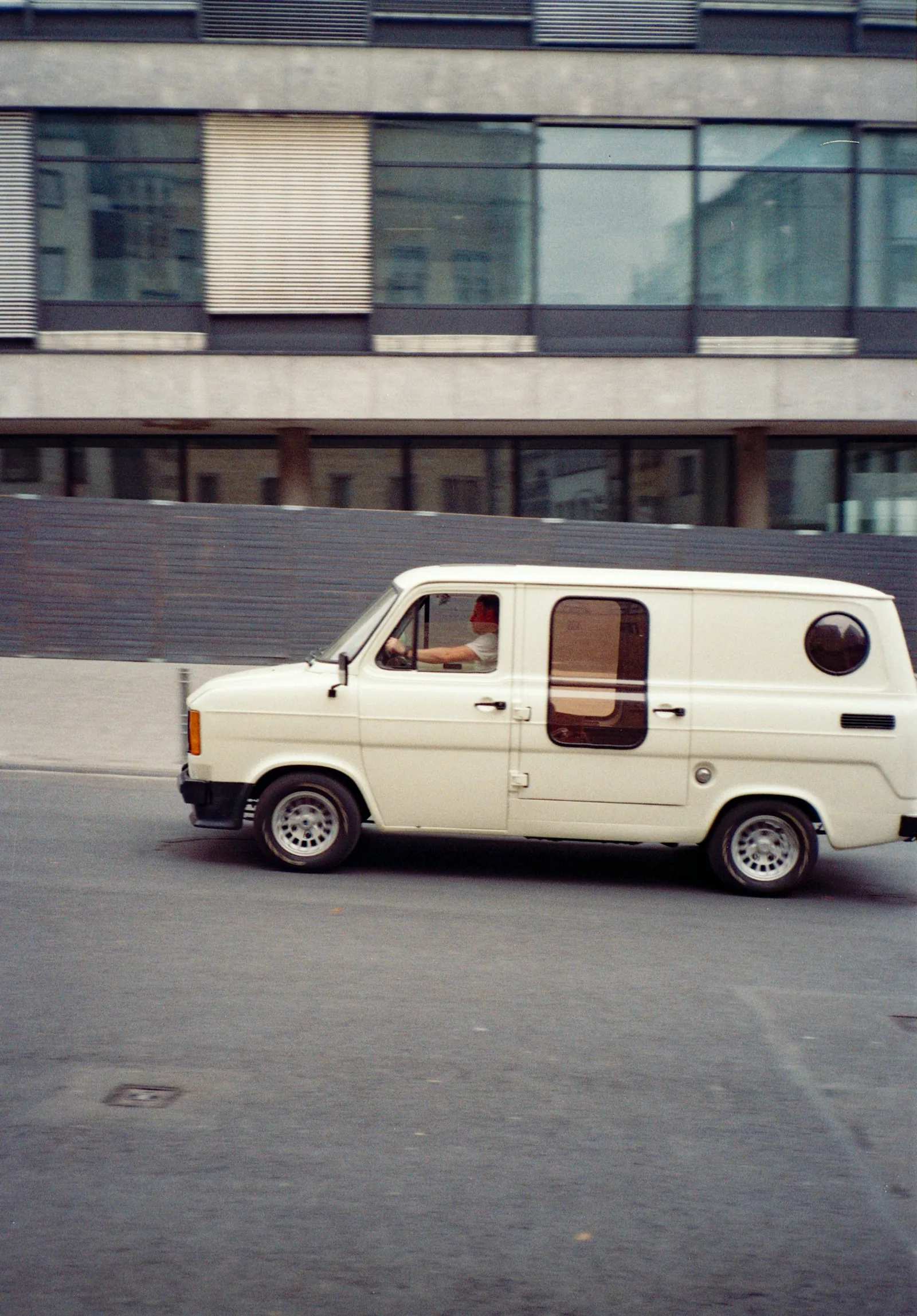 A plain white van parked on a street outside a modern office block