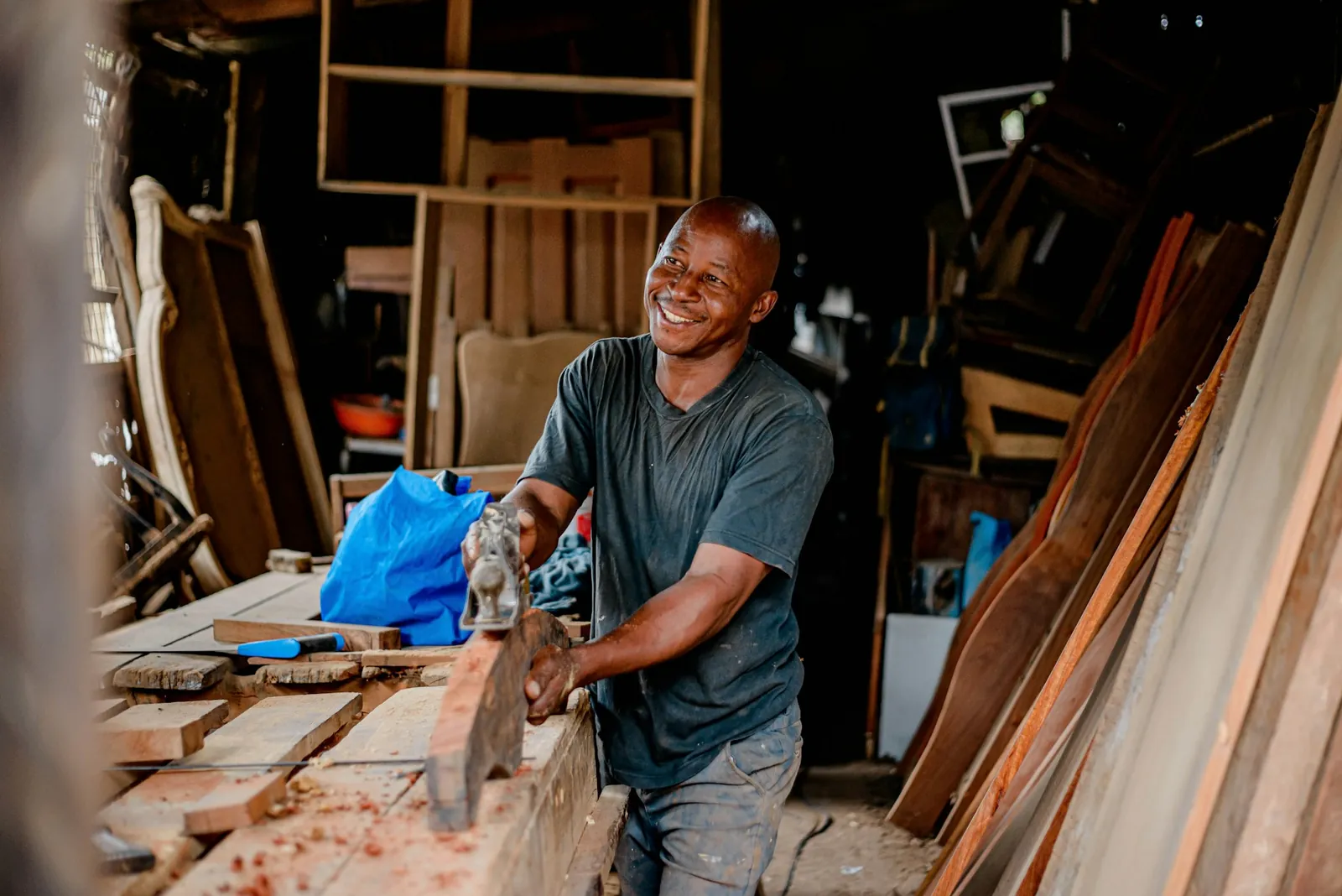 A joiner smiling as he planes a length of timber in his workshop