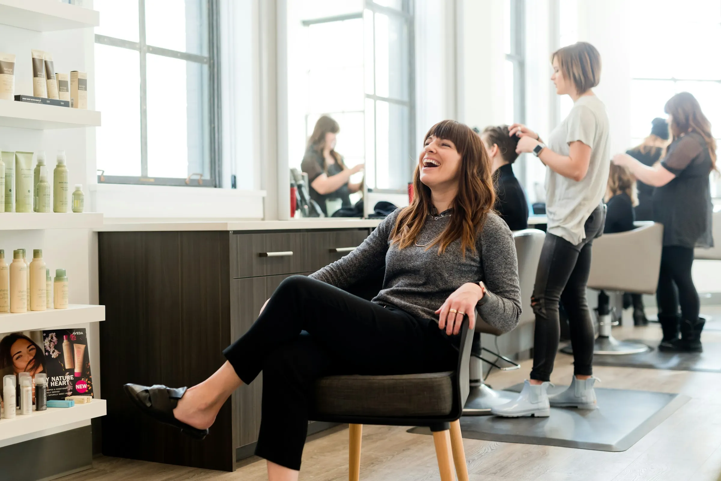 Claire laughing in a salon chair with the team working behind her