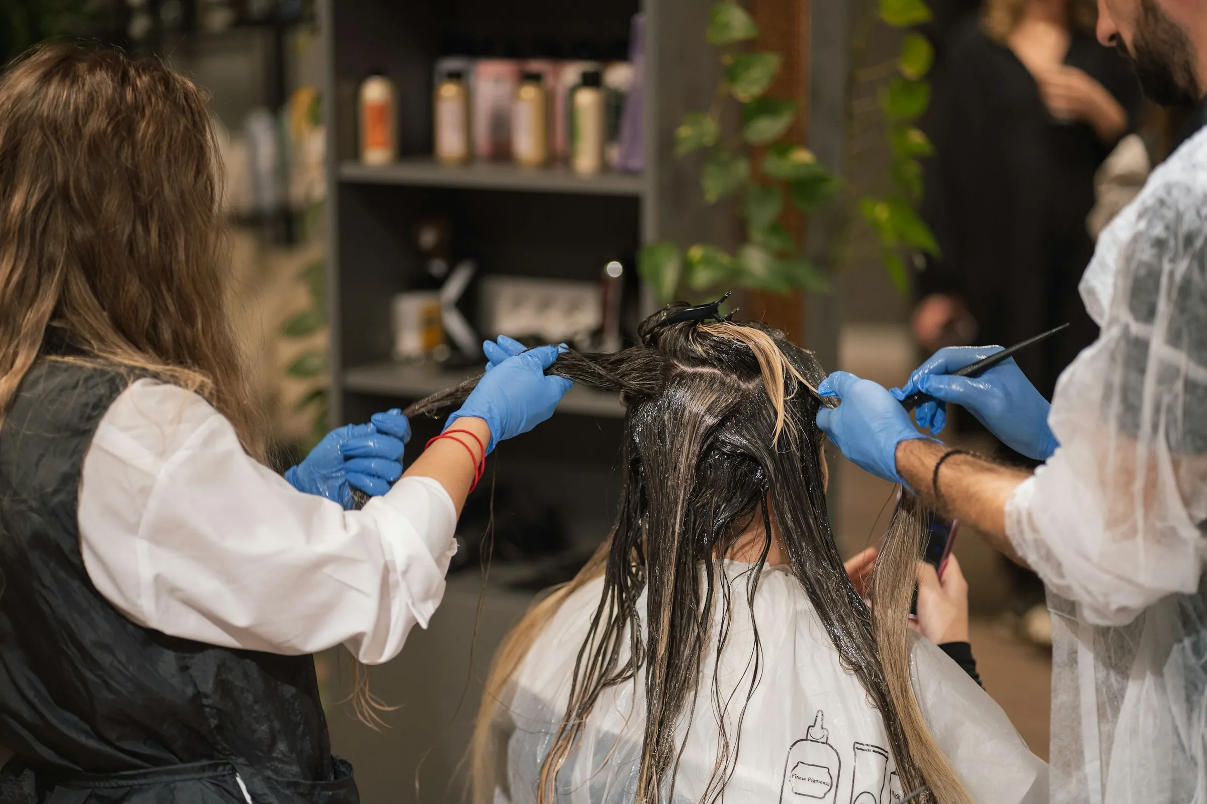 Two stylists in blue gloves painting colour through a client's hair