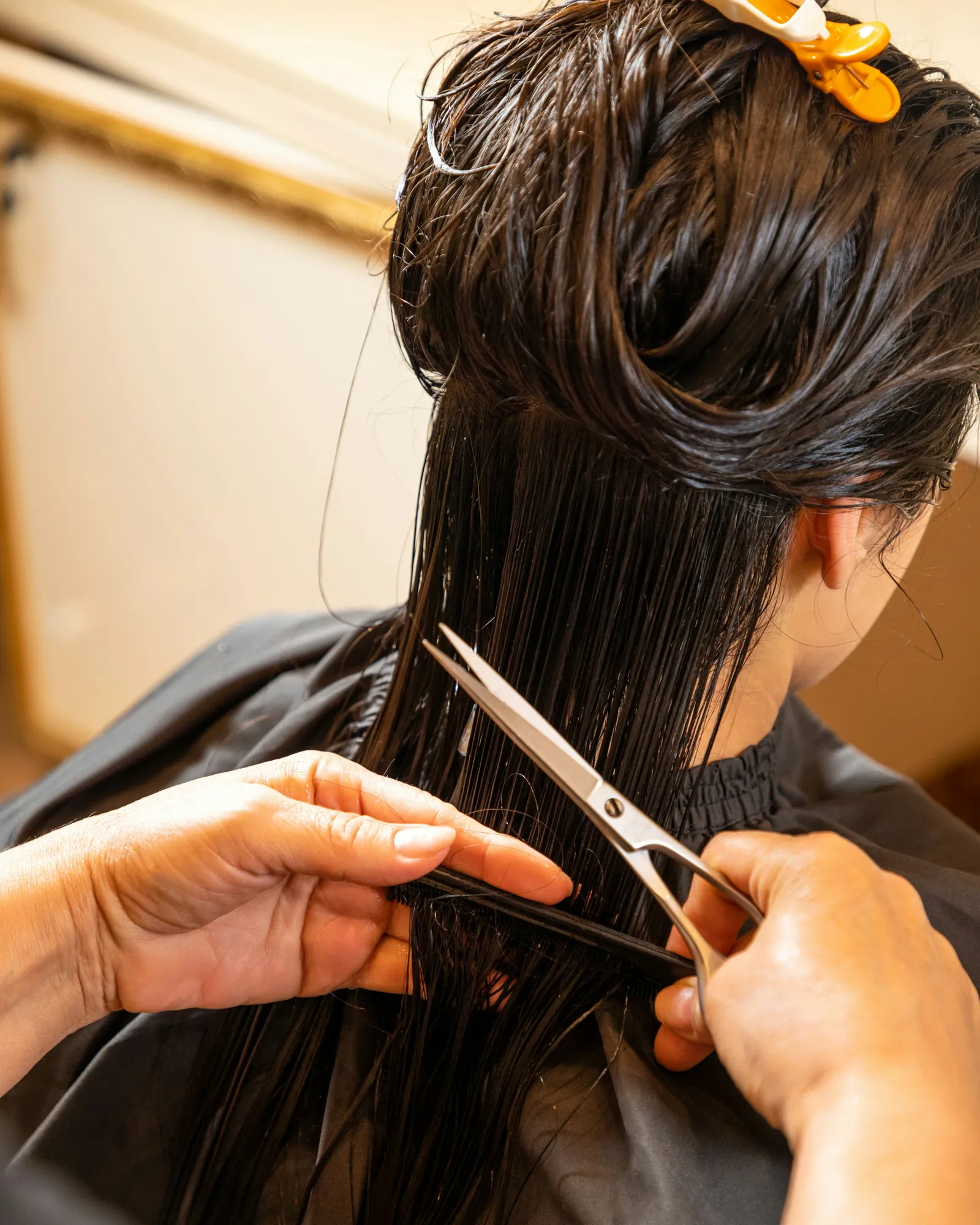 Scissors working through wet dark hair at the mirror