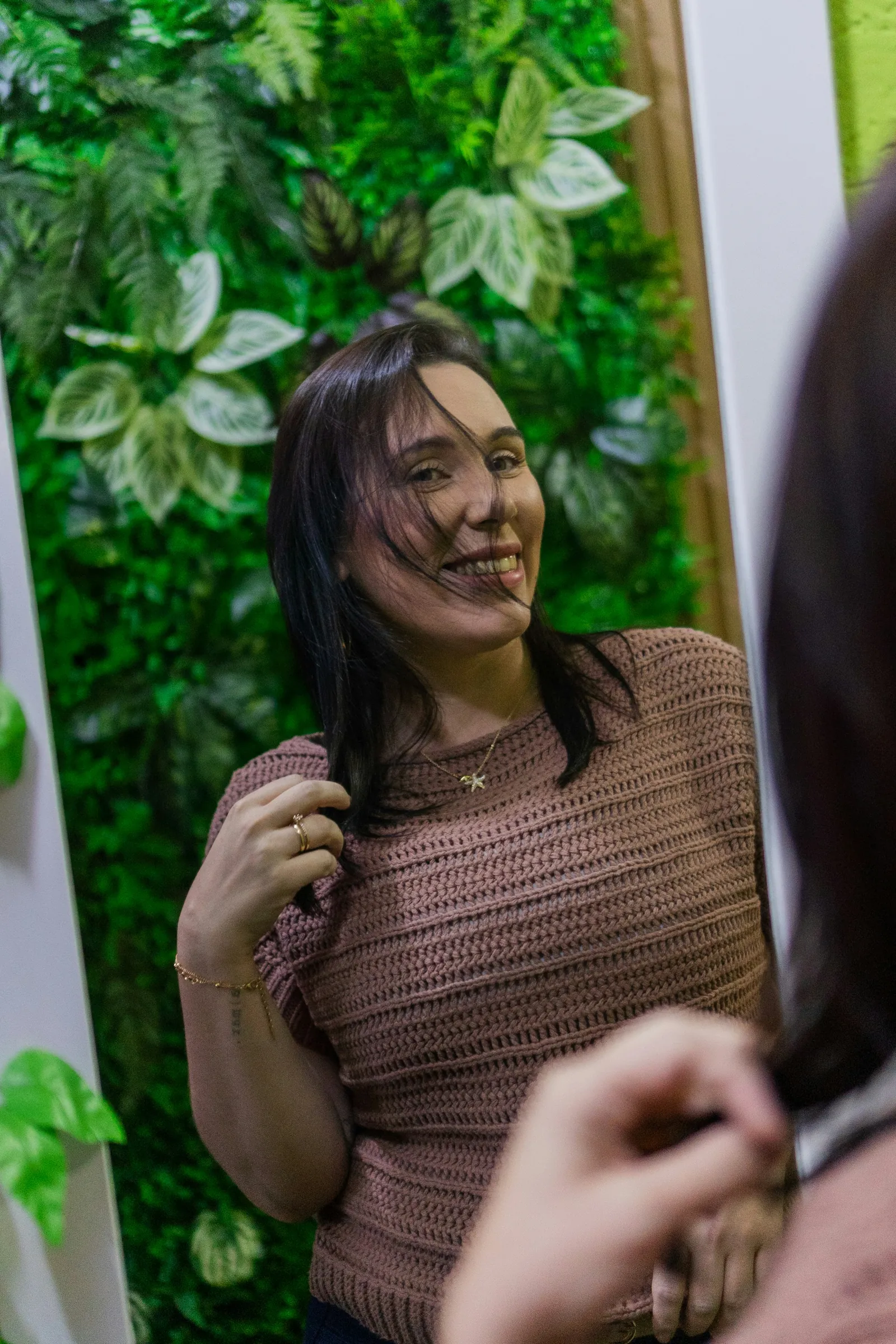 A client smiling at herself in the salon mirror by the plant wall