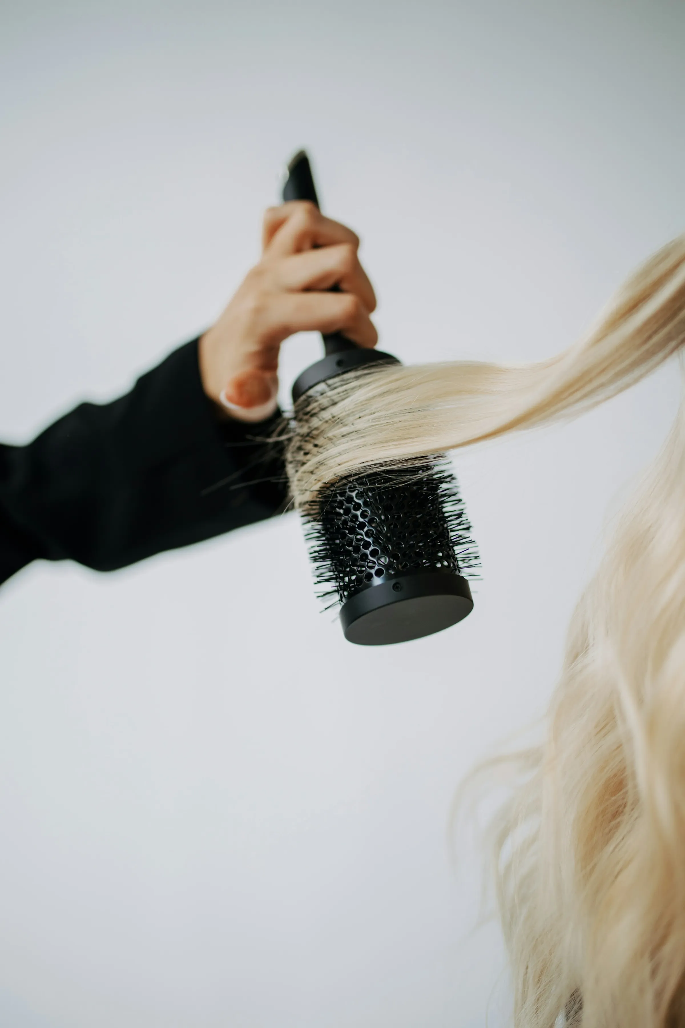 A round brush drawing a section of blonde hair out straight under the dryer