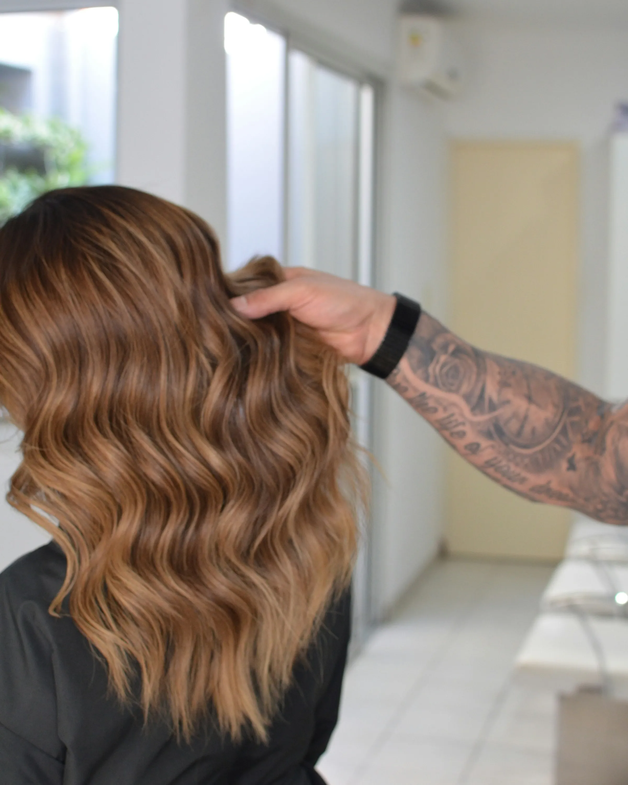 A stylist's hand lifting a section of bronze waved hair in the salon
